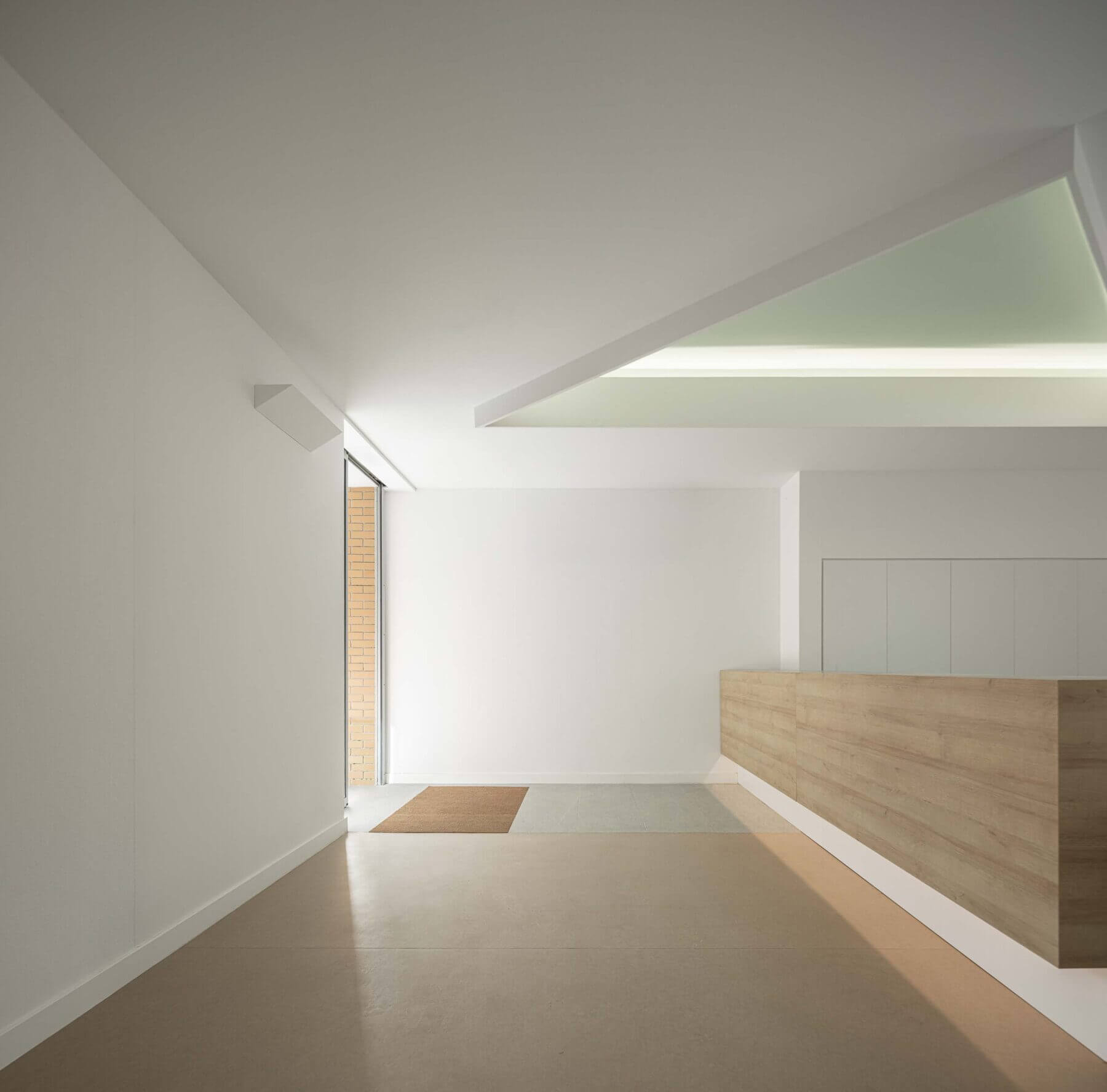 Receção: Balcão de atendimento em madeira, pavimento castanho e iluminação embutida no teto branco. — Associação Paralisia Cerebral de Odemira – APCO arquitetura Filipe Xavier Oliveira em Odemira