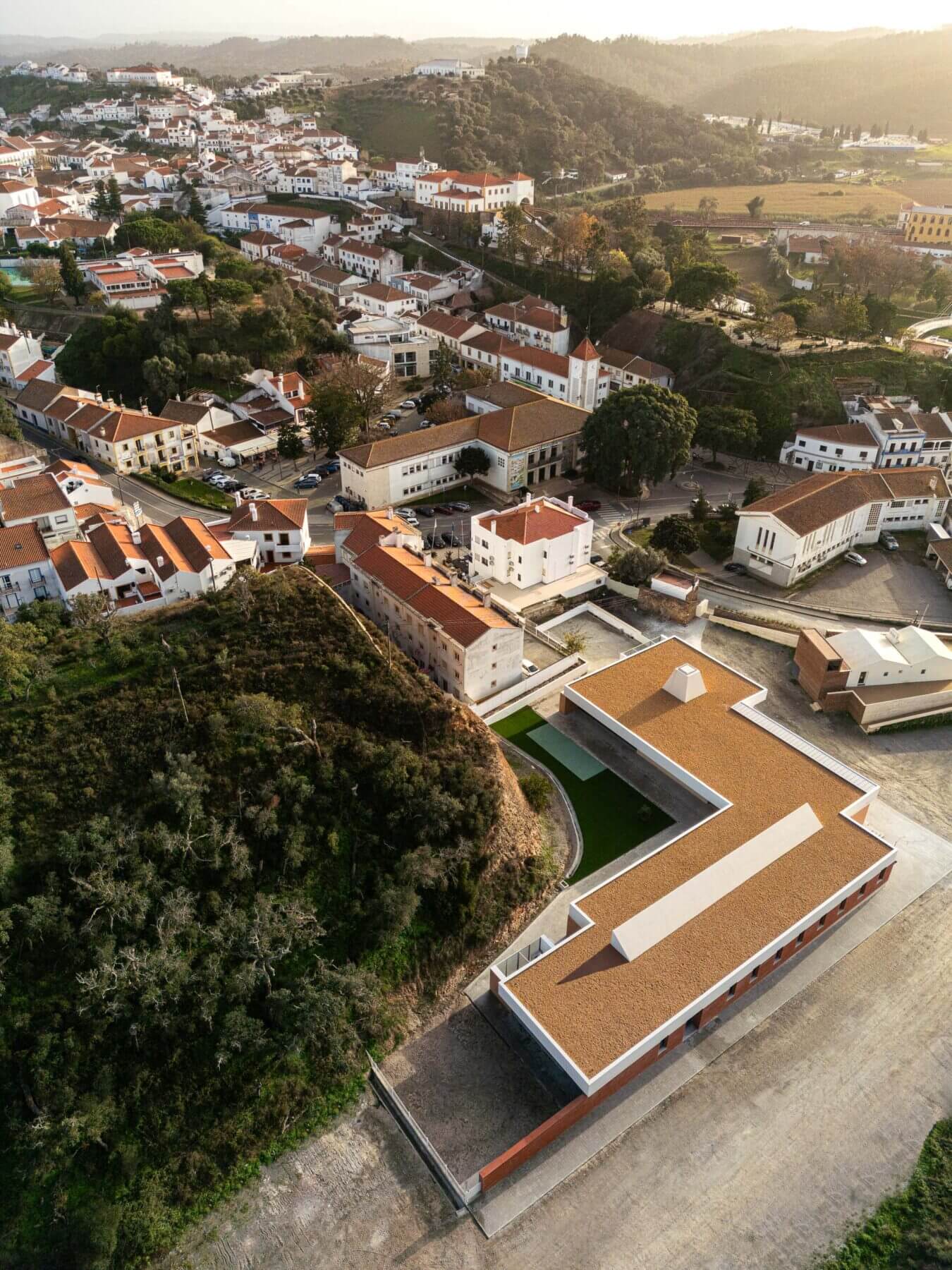 Edifício: Vista aérea da APCO integrada na vila de Odemira, com telhado castanho e zona ajardinada. — Associação Paralisia Cerebral de Odemira – APCO arquitetura Filipe Xavier Oliveira em Odemira
