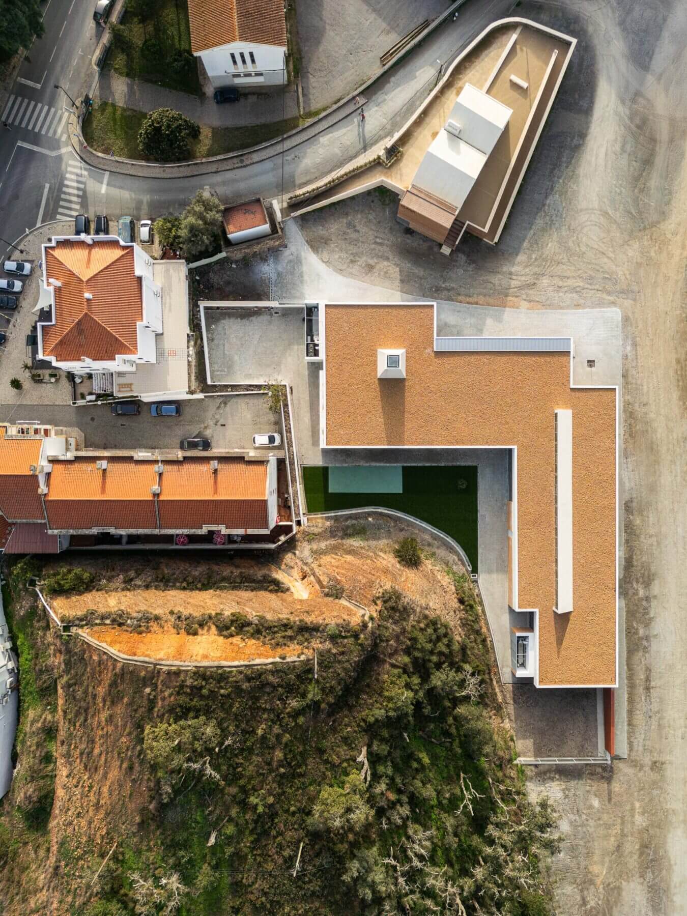 Edifício: Vista aérea superior da APCO, com telhado castanho, pátio interior e envolvente natural. — Associação Paralisia Cerebral de Odemira – APCO arquitetura Filipe Xavier Oliveira em Odemira