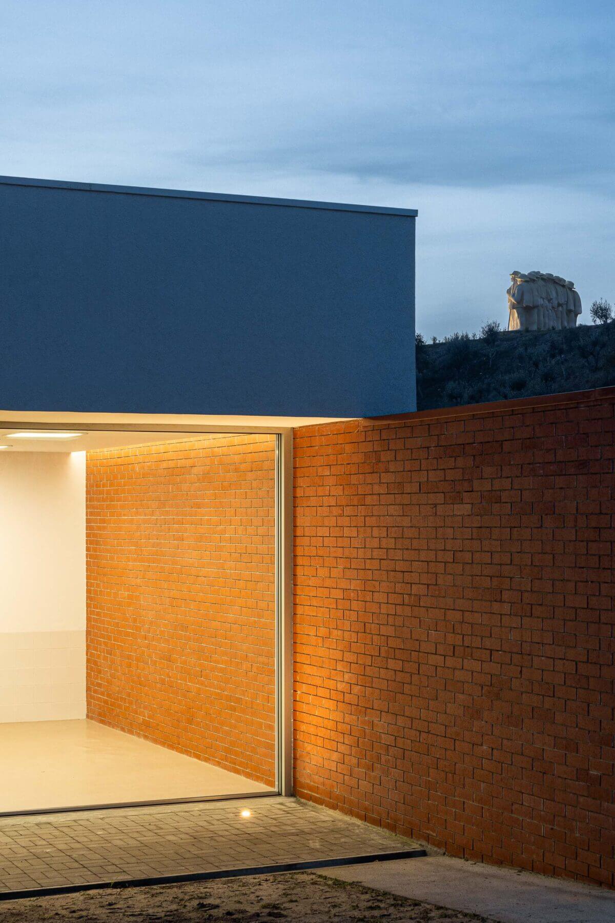 Pátio: Detalhe da fachada em tijolo da APCO com iluminação e vista para o interior com azulejos brancos. — Associação Paralisia Cerebral de Odemira – APCO arquitetura Filipe Xavier Oliveira em Odemira