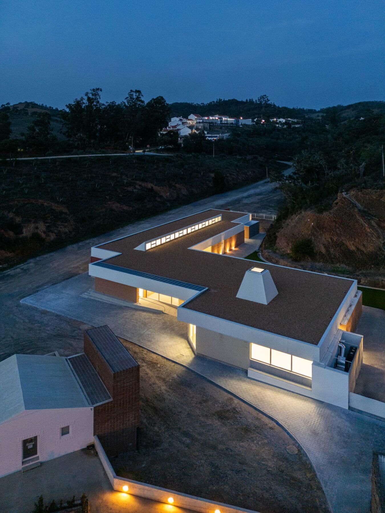 Edifício: Vista aérea noturna da APCO, com iluminação interior e exterior, e a paisagem envolvente. — Associação Paralisia Cerebral de Odemira – APCO arquitetura Filipe Xavier Oliveira em Odemira