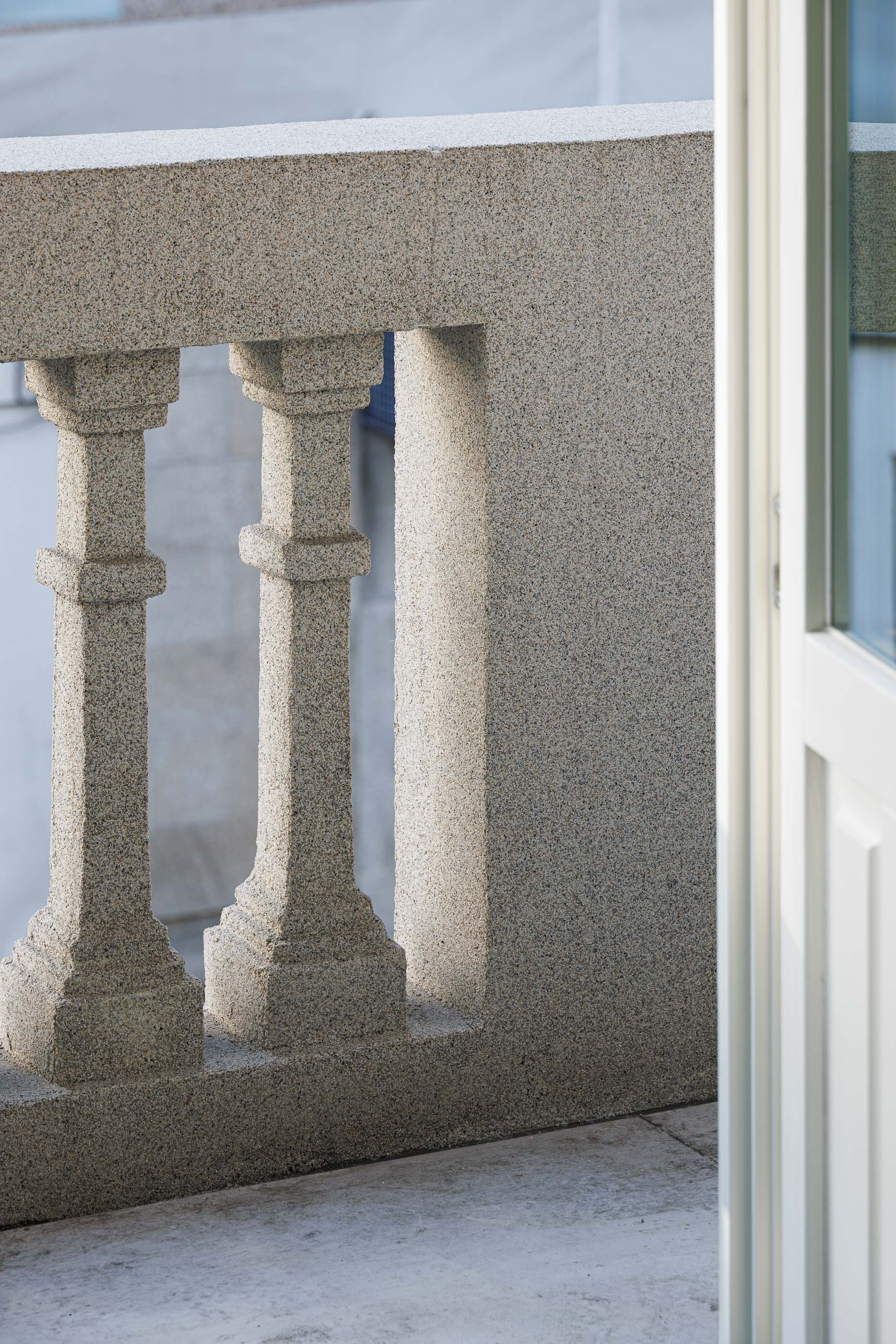 Varanda: Pormenor da balaustrada em granito da varanda, com porta branca entreaberta. — Apartamentos Vitória arquitetura Floret Arquitectura em Viseu
