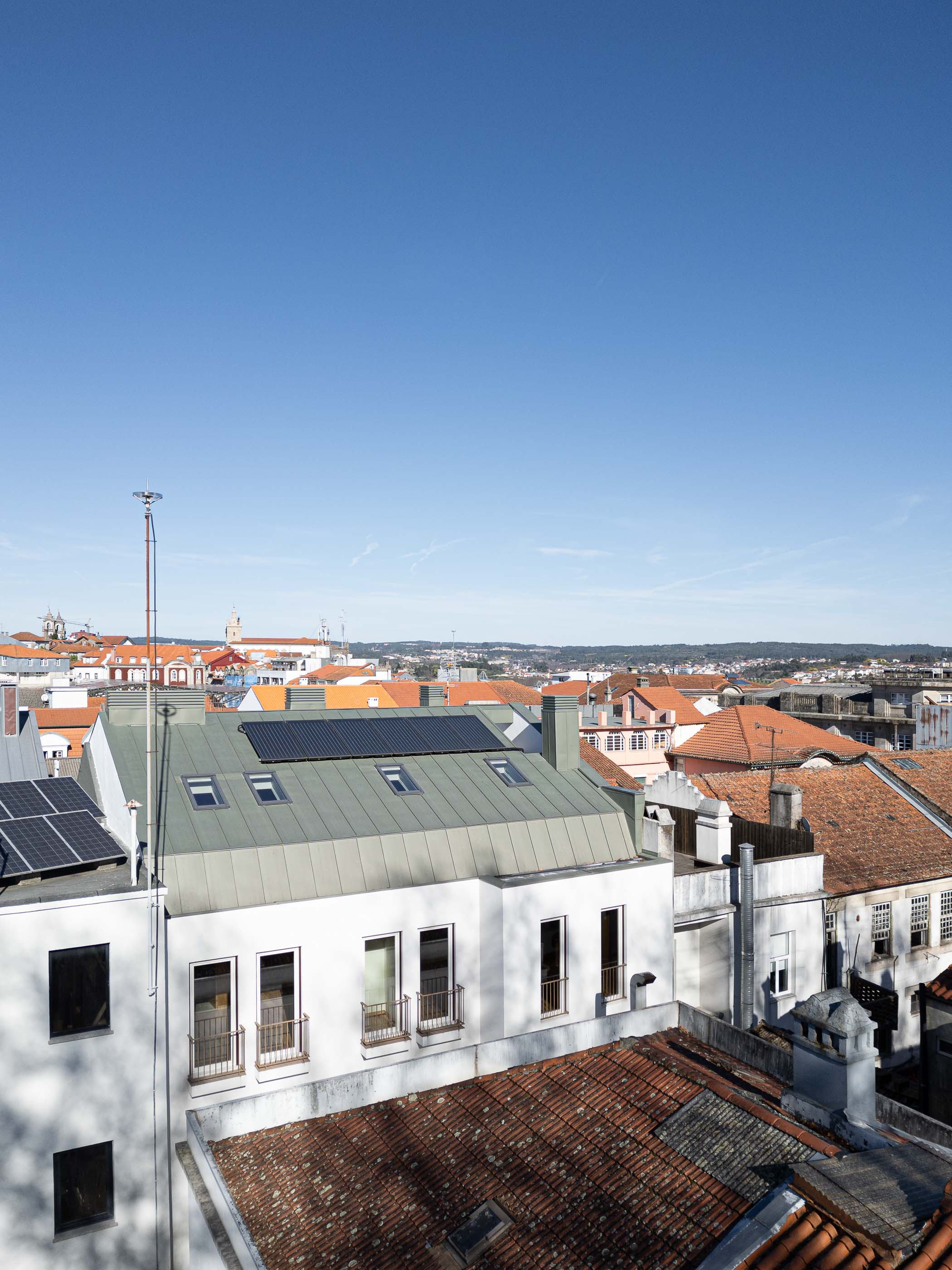 Exterior: Vista aérea do edifício com telhado cinzento, painéis solares e vista panorâmica sobre Viseu. — Apartamentos Vitória arquitetura Floret Arquitectura em Viseu