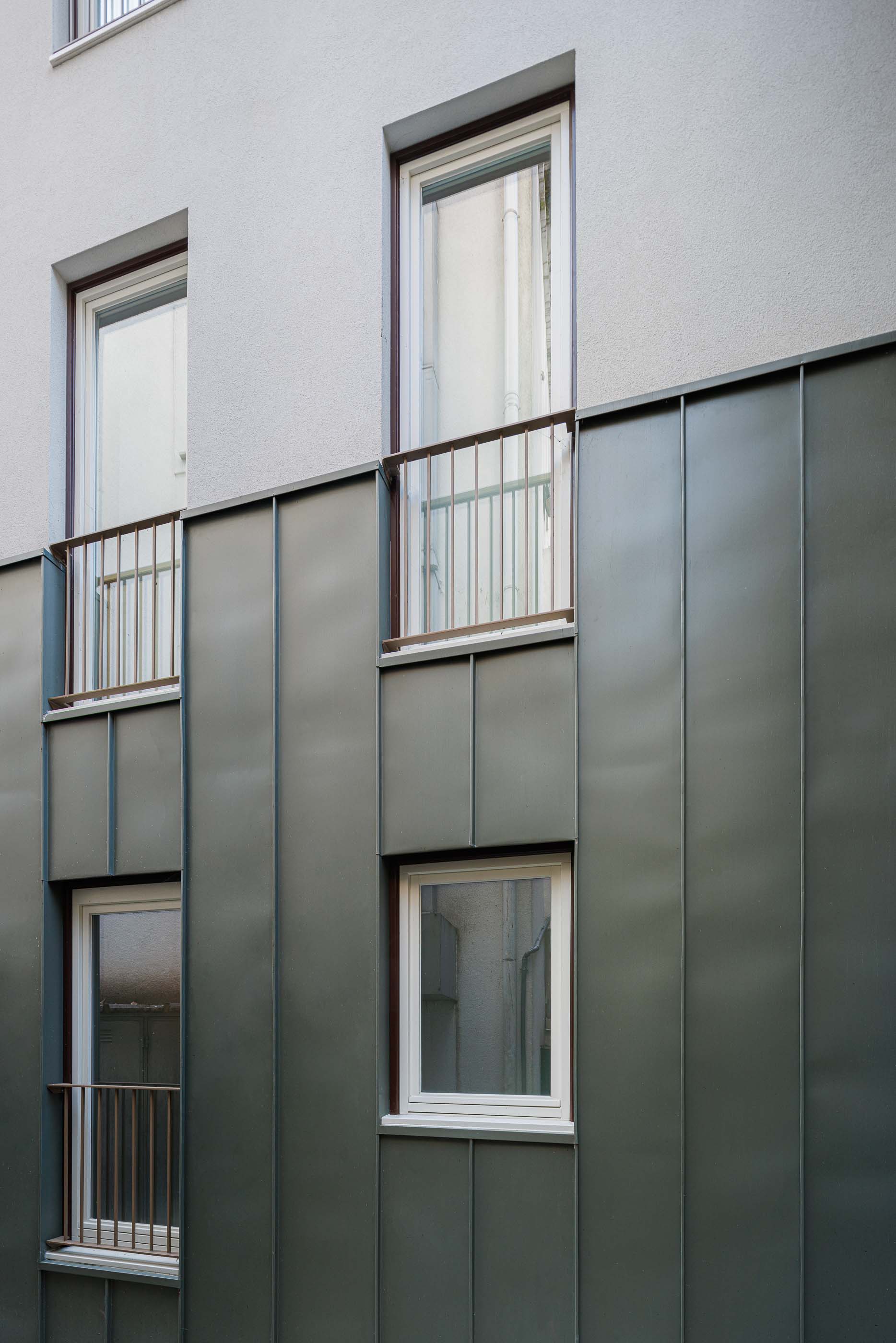 Exterior: Detalhe da fachada lateral com revestimento metálico cinzento, janelas brancas e varandas. — Apartamentos Vitória arquitetura Floret Arquitectura em Viseu