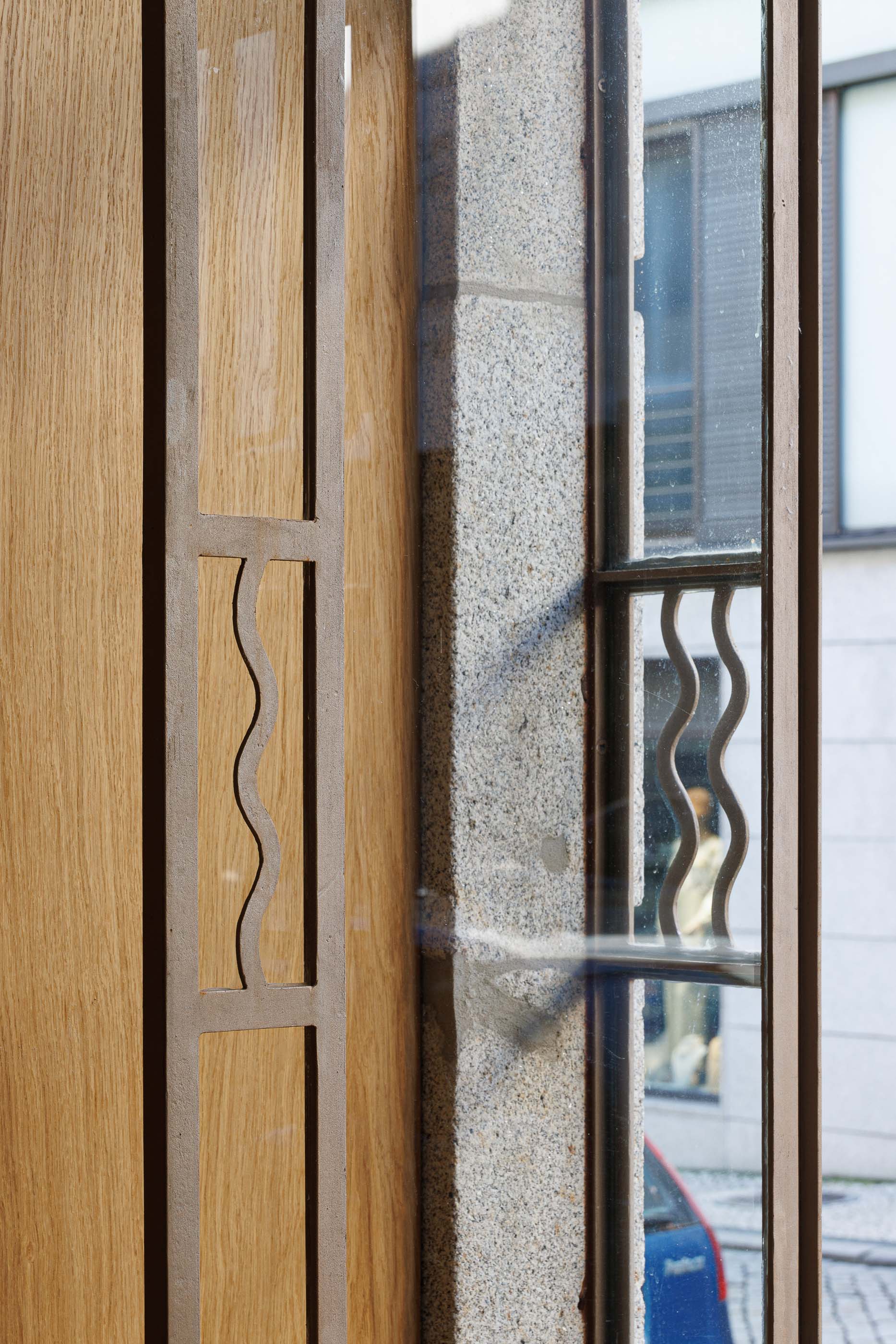 Hall de entrada: Detalhe da porta de entrada envidraçada com padrão ondulado e caixilharia em madeira clara. — Apartamentos Vitória arquitetura Floret Arquitectura em Viseu