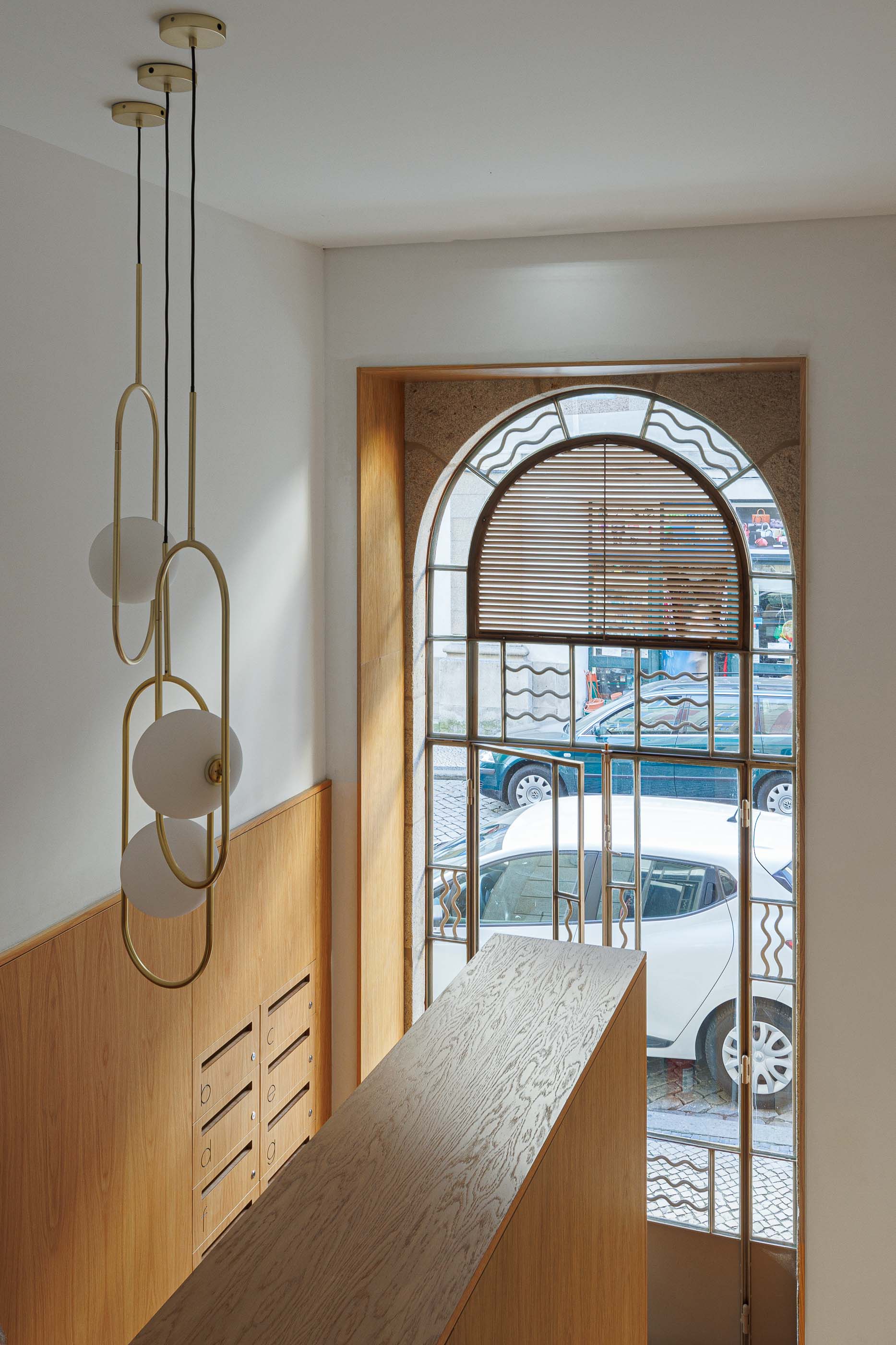 Hall de entrada: Vista superior da porta envidraçada, caixas de correio e candeeiros suspensos. — Apartamentos Vitória arquitetura Floret Arquitectura em Viseu