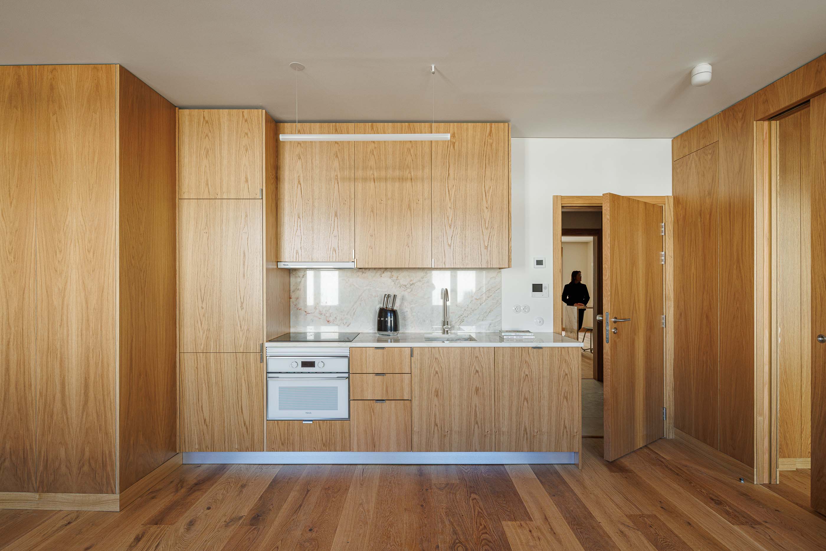 Cozinha: Armários em madeira clara, bancada em mármore e pavimento em madeira num apartamento moderno. — Apartamentos Vitória arquitetura Floret Arquitectura em Viseu