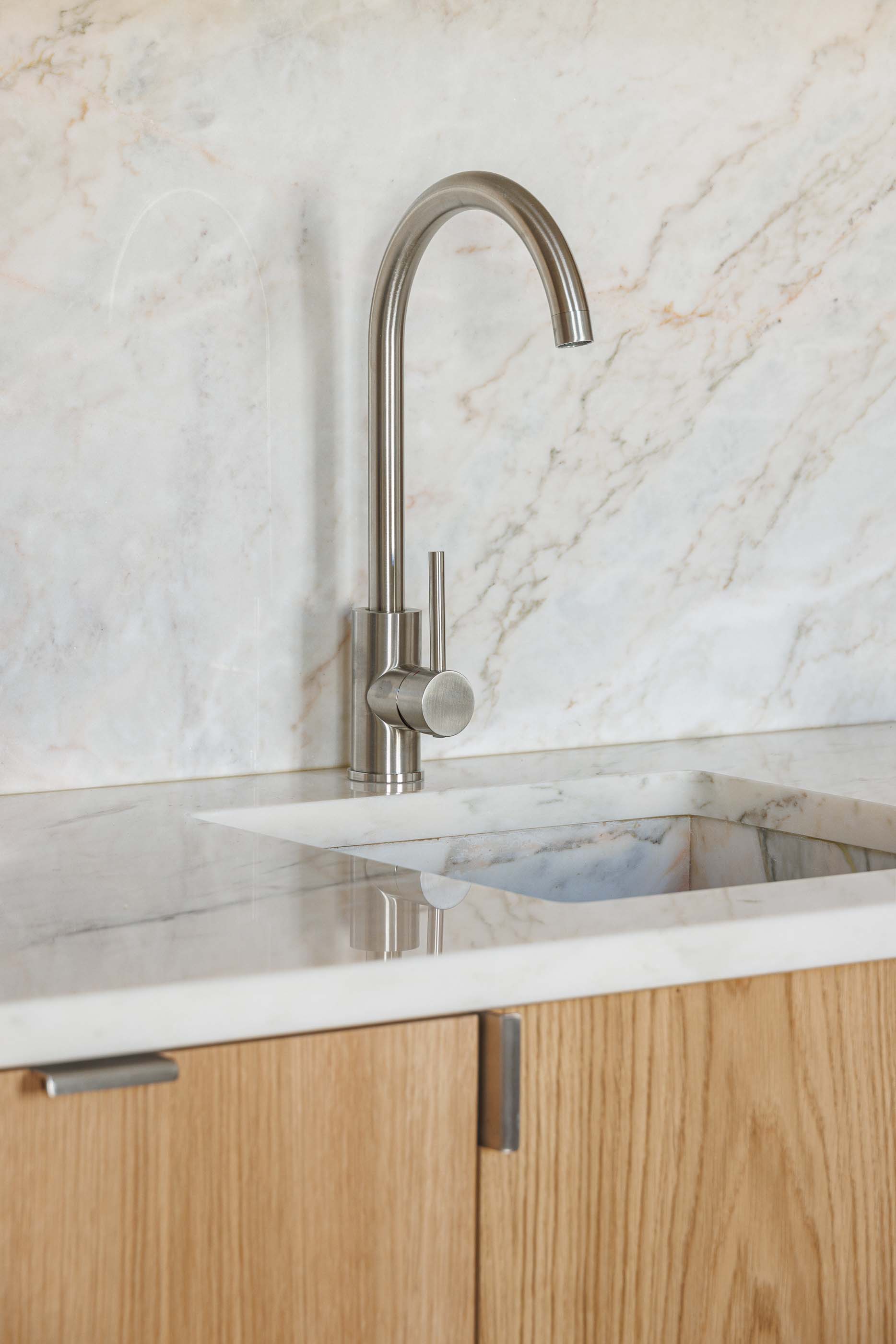 Cozinha: Detalhe da torneira em aço inoxidável e bancada em mármore com armários em madeira clara. — Apartamentos Vitória arquitetura Floret Arquitectura em Viseu
