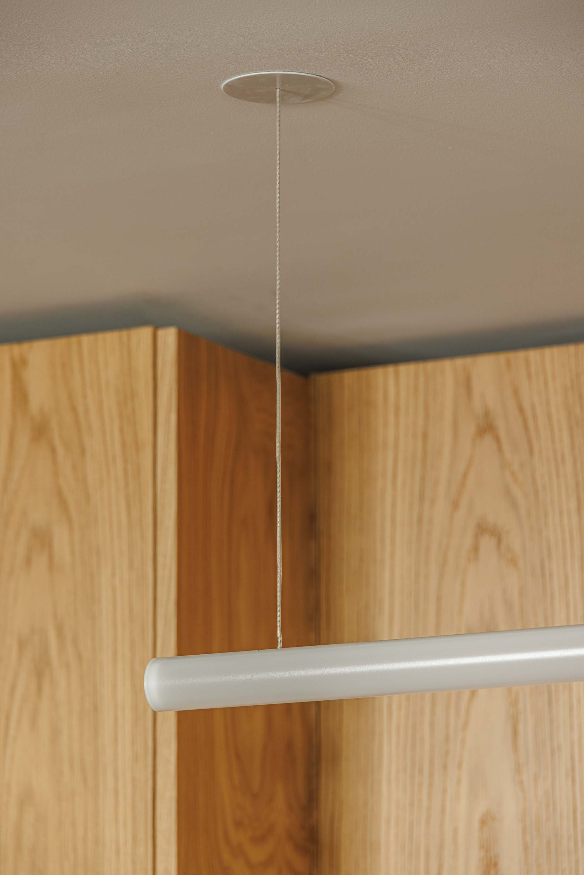 Cozinha: Candeeiro tubular suspenso sobre armários em madeira clara. — Apartamentos Vitória arquitetura Floret Arquitectura em Viseu