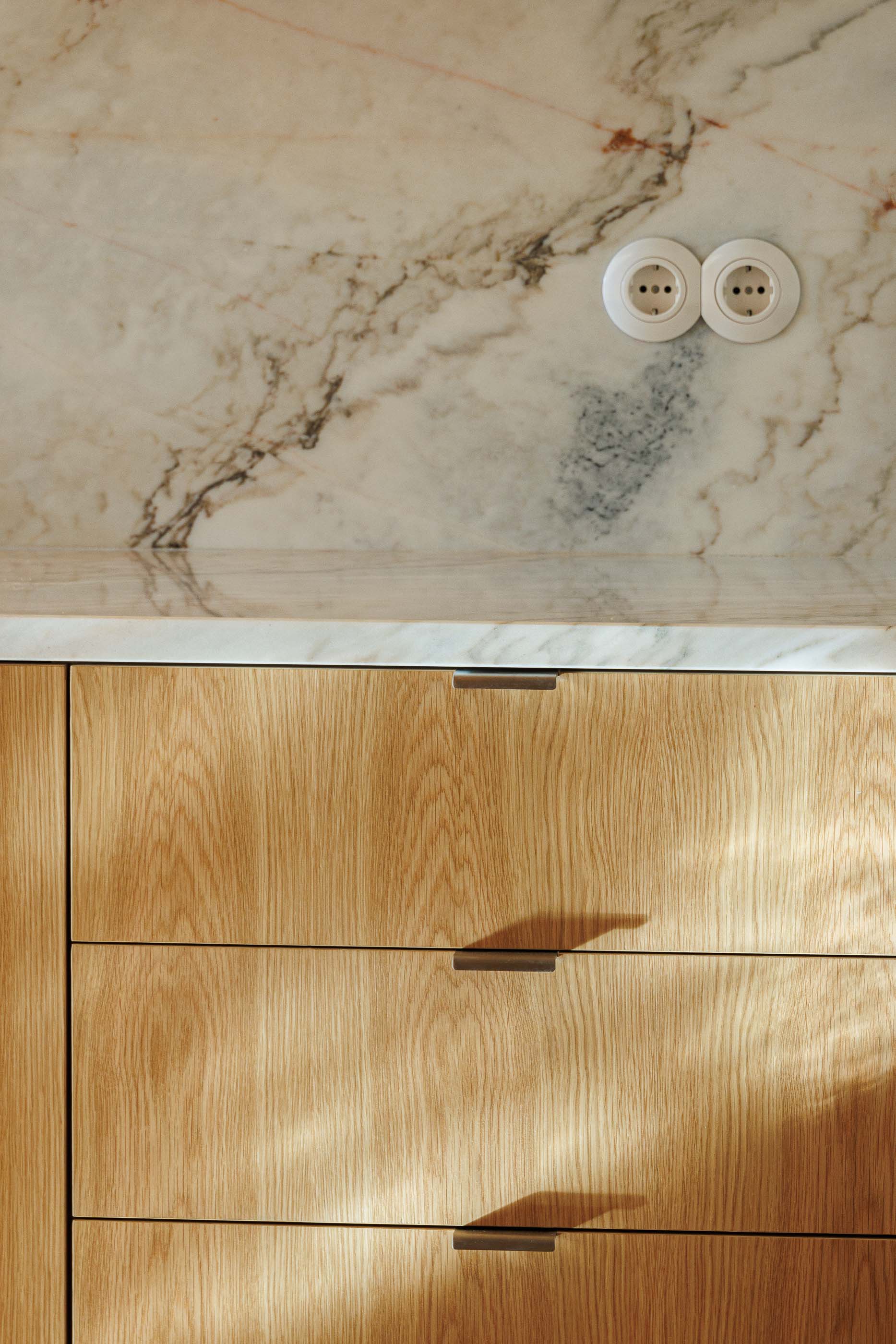 Cozinha: Detalhe da bancada em mármore com tomadas e armários em madeira clara. — Apartamentos Vitória arquitetura Floret Arquitectura em Viseu