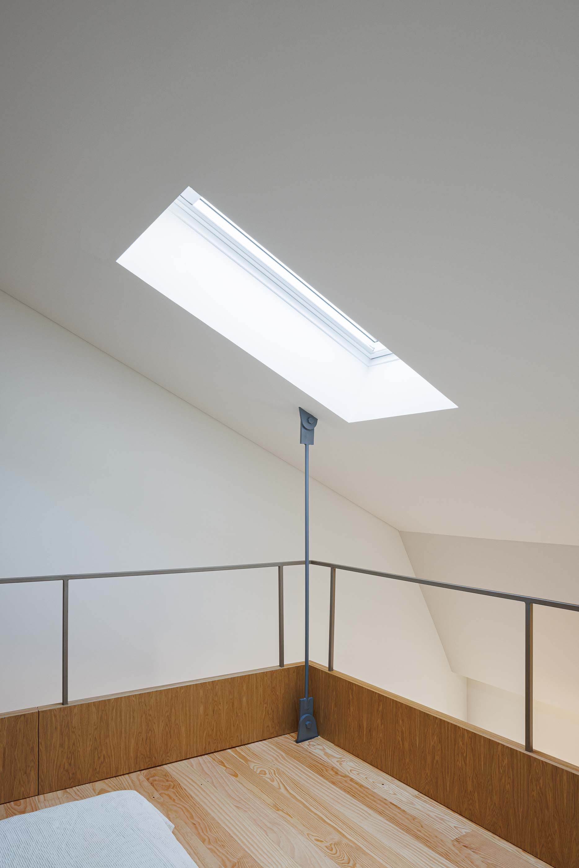 Mezzanine: Sótão com claraboia, pavimento em madeira clara e guarda-corpo metálico. — Apartamentos Vitória arquitetura Floret Arquitectura em Viseu