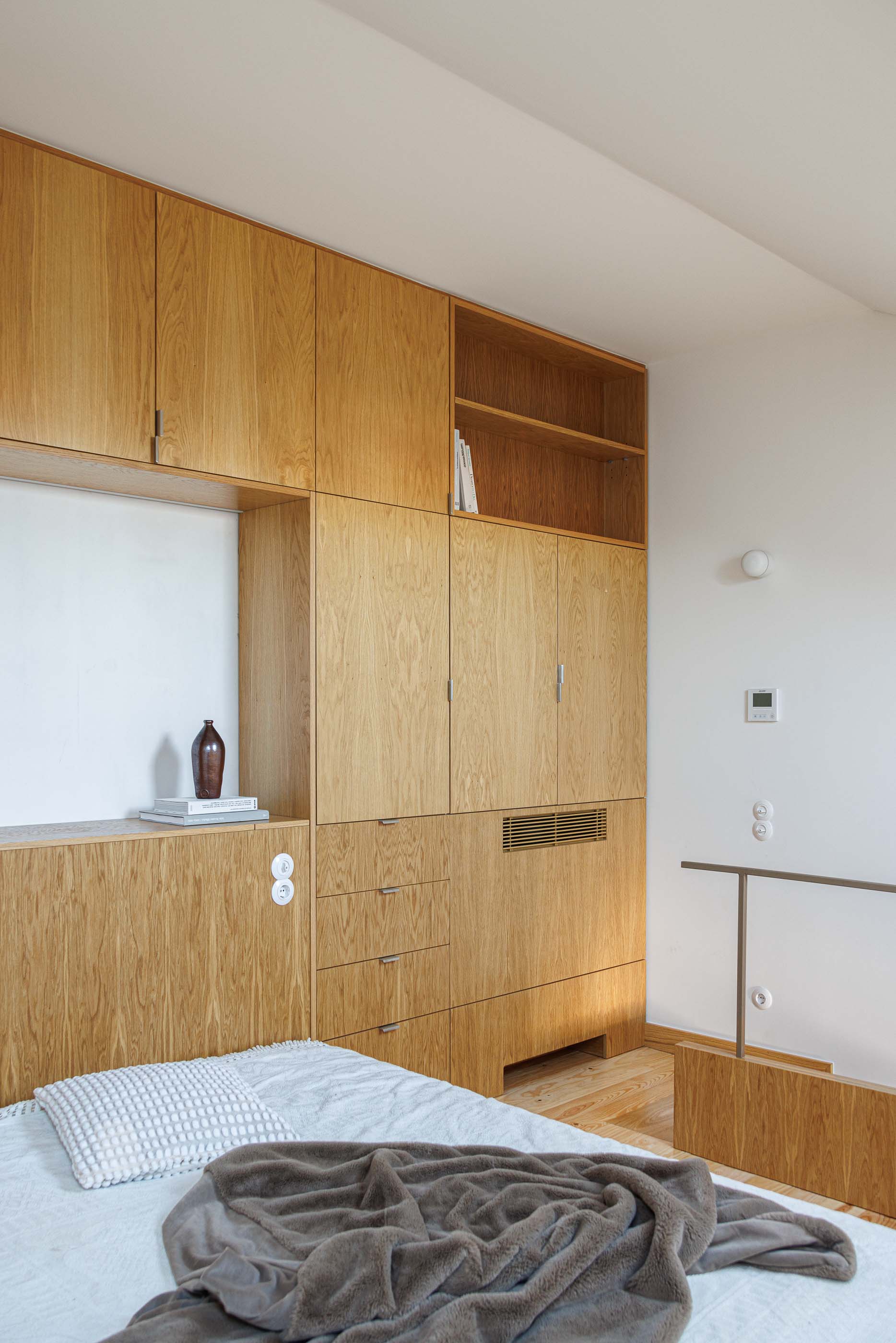 Quarto: Cama com roupa de cama clara, armários embutidos em madeira clara e mezzanine. — Apartamentos Vitória arquitetura Floret Arquitectura em Viseu