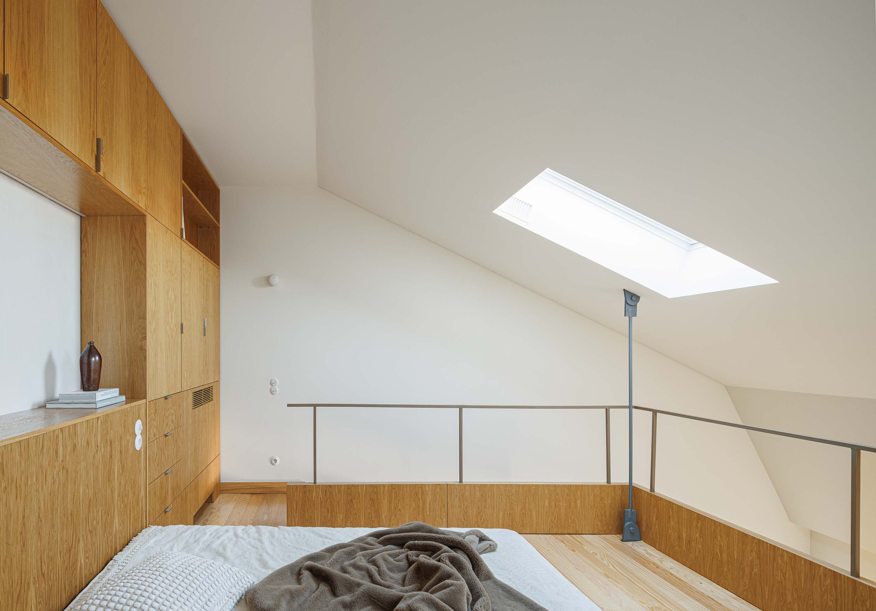 Quarto: Vista geral do quarto com cama, armários embutidos, claraboia e mezzanine. — Apartamentos Vitória arquitetura Floret Arquitectura em Viseu