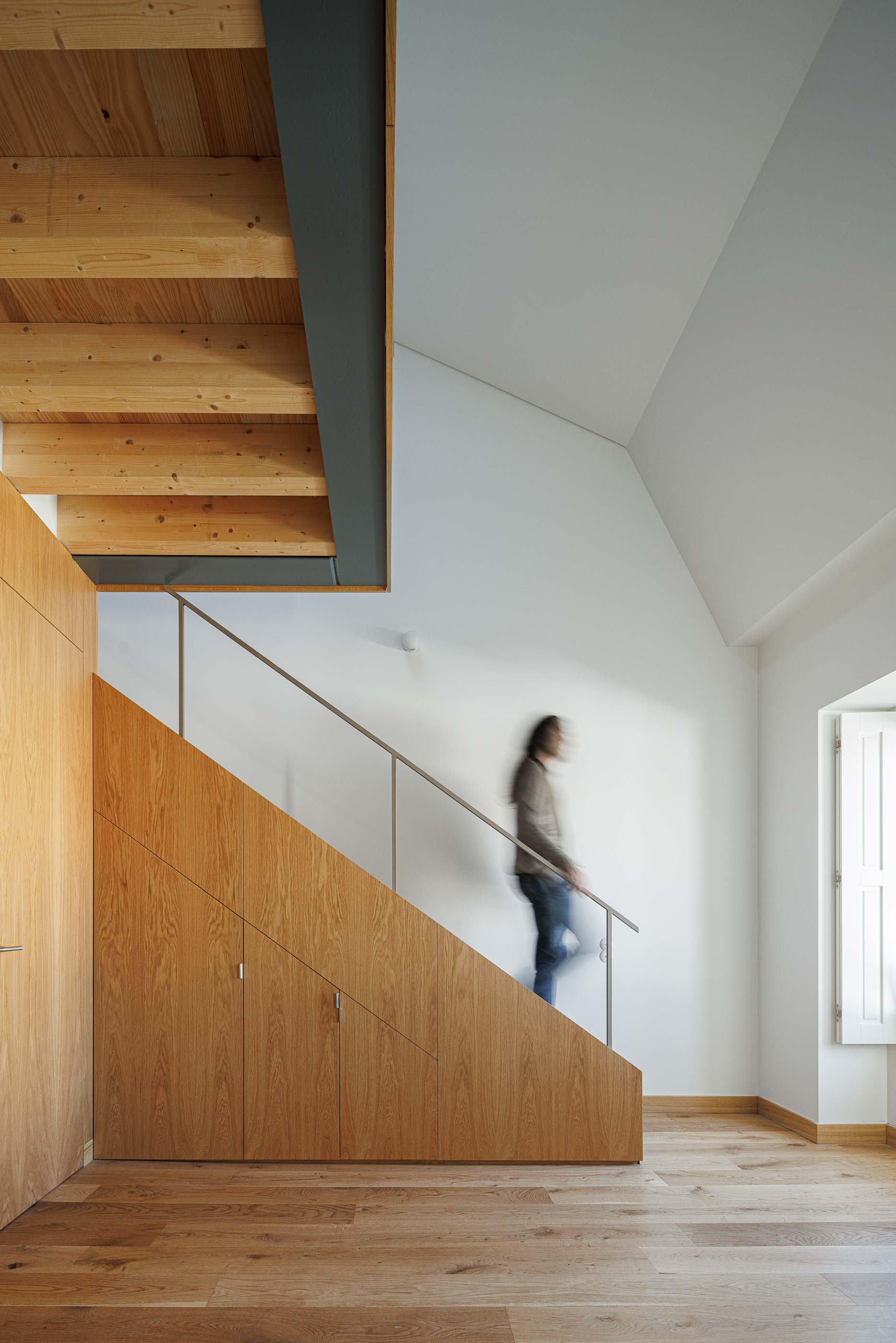 Escadas: Escadas em madeira clara com guarda-corpo metálico e pessoa a descer. — Apartamentos Vitória arquitetura Floret Arquitectura em Viseu
