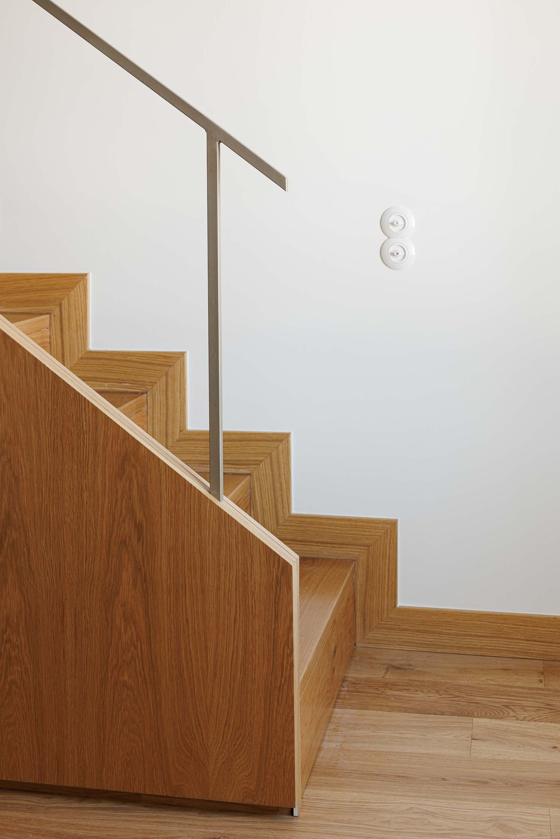 Escadas: Detalhe das escadas em madeira clara com guarda-corpo metálico e interruptores rotativos. — Apartamentos Vitória arquitetura Floret Arquitectura em Viseu
