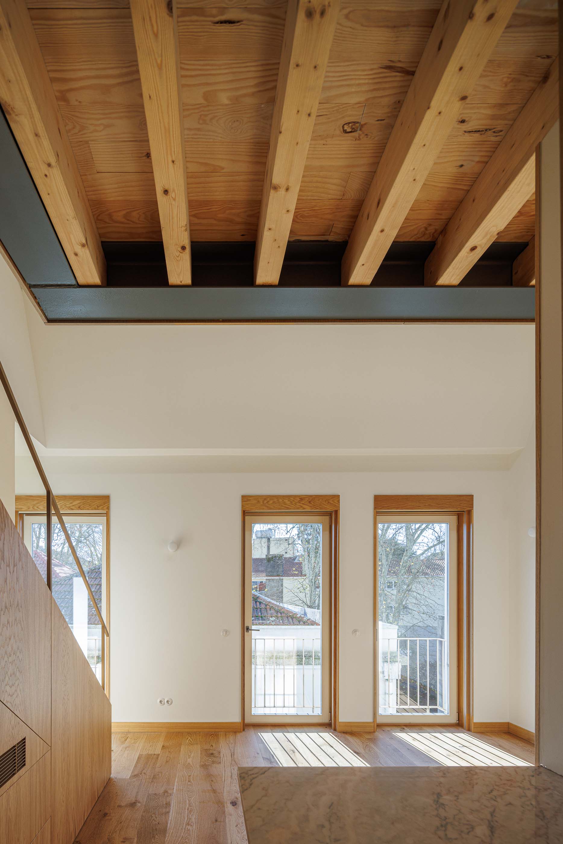 Sala de estar: Escadas em madeira clara, teto com vigas expostas e janelas com varanda. — Apartamentos Vitória arquitetura Floret Arquitectura em Viseu