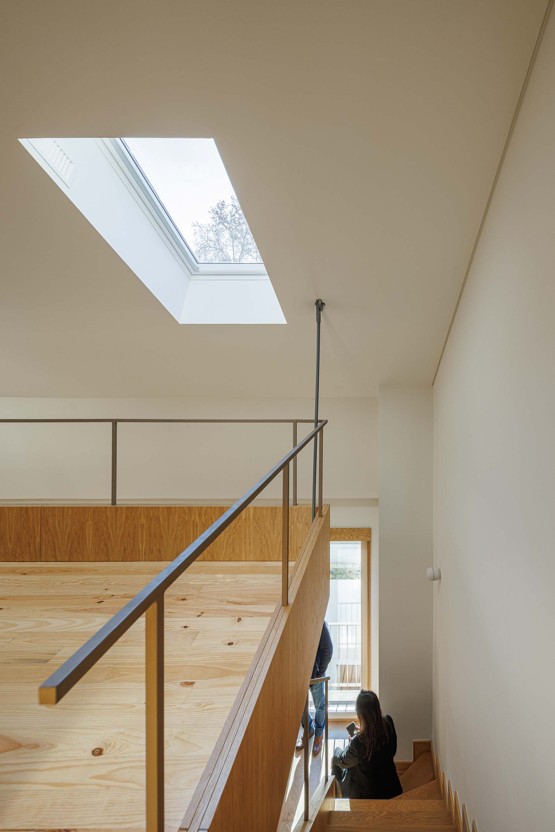 Mezzanine: Pessoas a subir escadas para mezzanine com claraboia e guarda-corpo metálico. — Apartamentos Vitória arquitetura Floret Arquitectura em Viseu