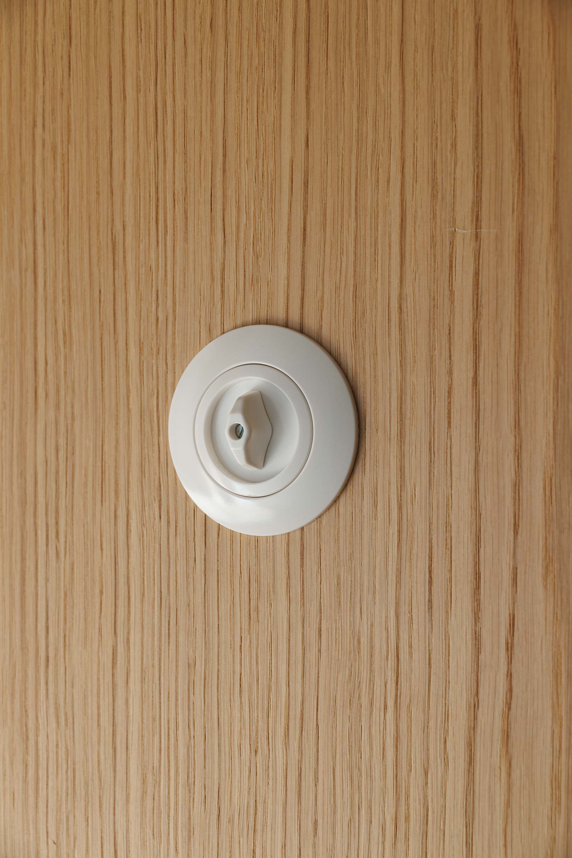 Detalhe: Interruptor rotativo branco numa parede em madeira clara. — Apartamentos Vitória arquitetura Floret Arquitectura em Viseu