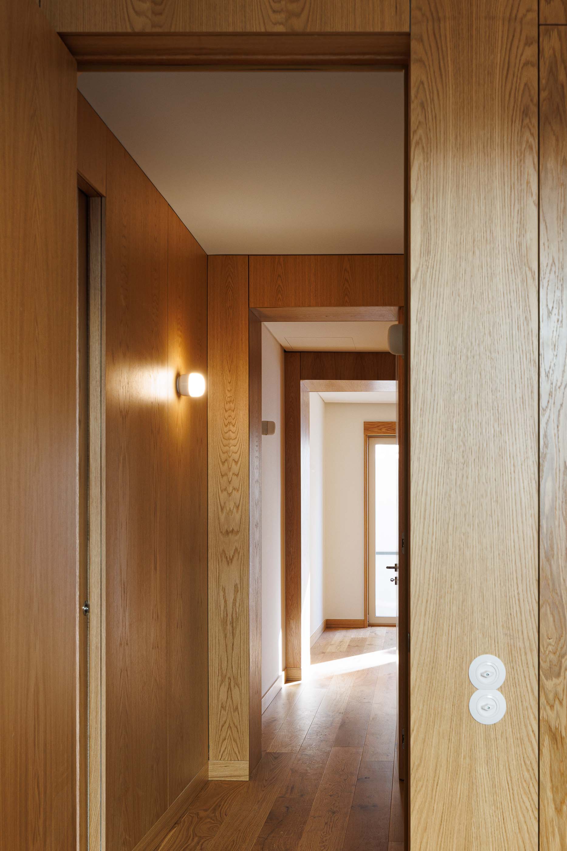 Corredor: Corredor com armários embutidos em madeira clara e candeeiros de parede. — Apartamentos Vitória arquitetura Floret Arquitectura em Viseu