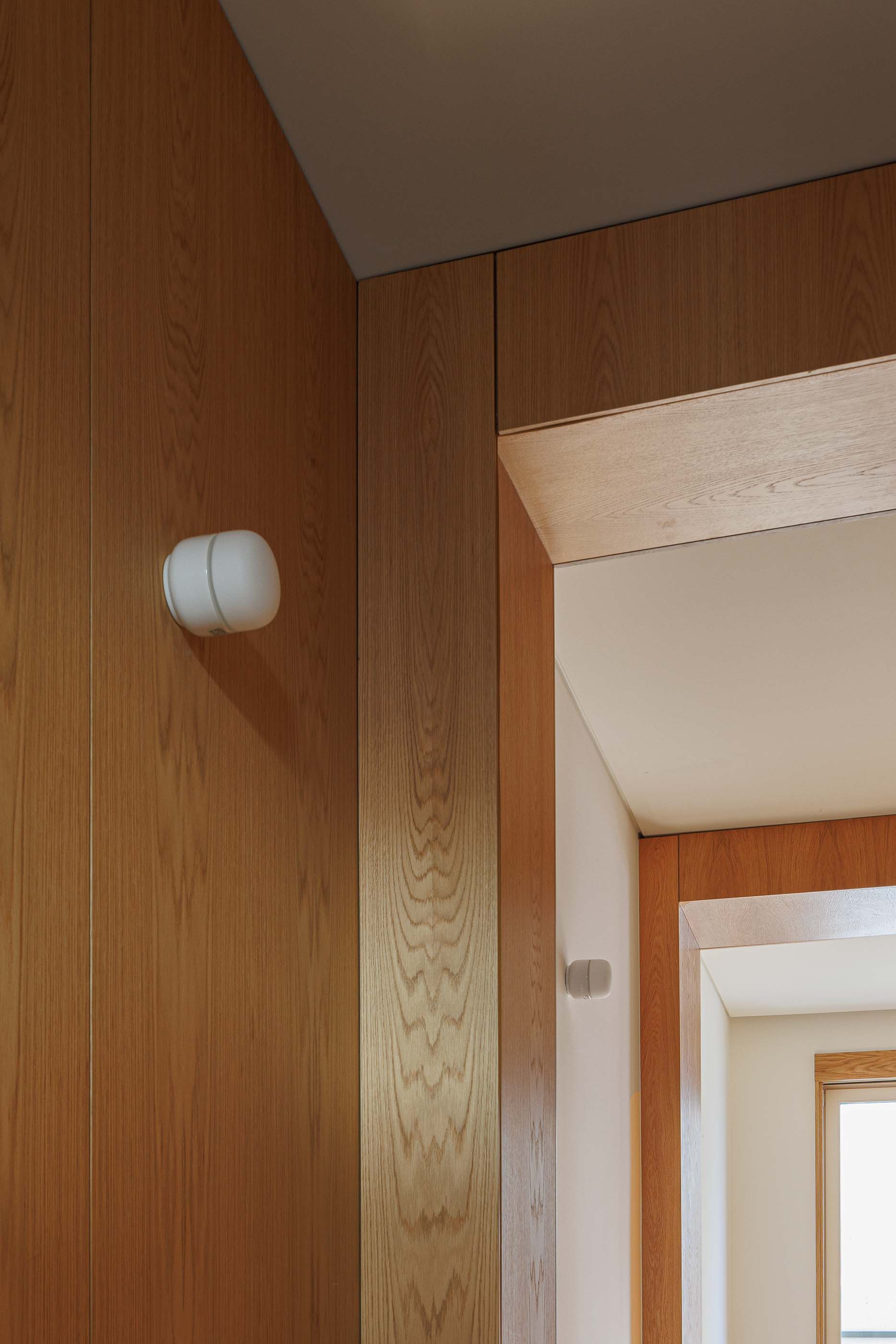 Corredor: Detalhe do corredor com candeeiro de parede e caixilharia em madeira clara. — Apartamentos Vitória arquitetura Floret Arquitectura em Viseu