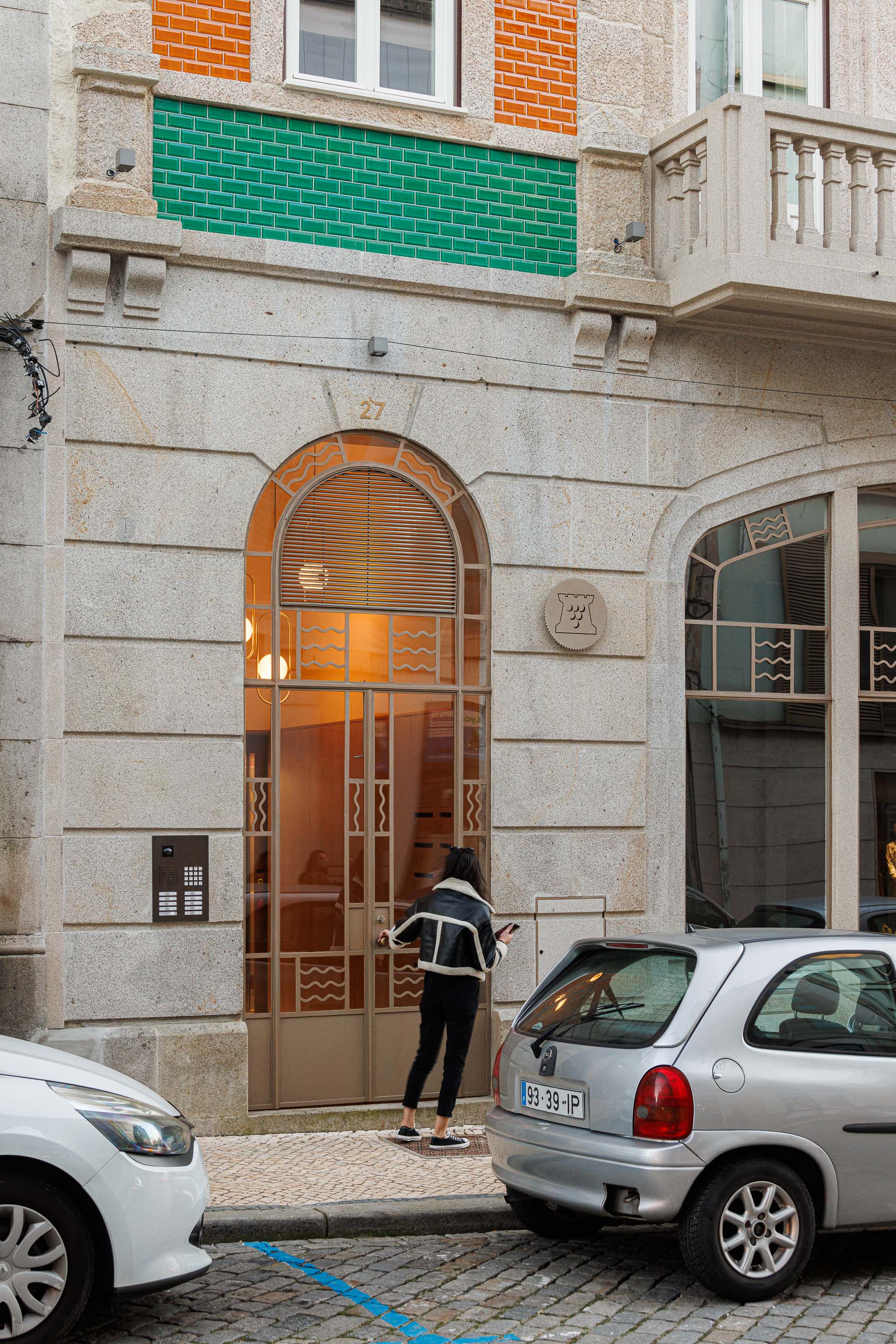 Exterior: Fachada do edifício com porta de entrada em arco e pessoa a entrar. — Apartamentos Vitória arquitetura Floret Arquitectura em Viseu