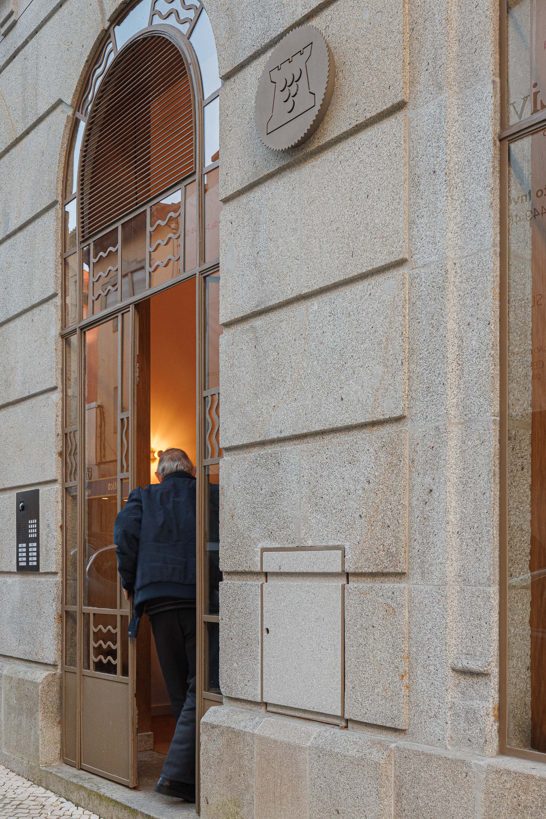 Exterior: Detalhe da porta de entrada em arco com pessoa a entrar no edifício. — Apartamentos Vitória arquitetura Floret Arquitectura em Viseu