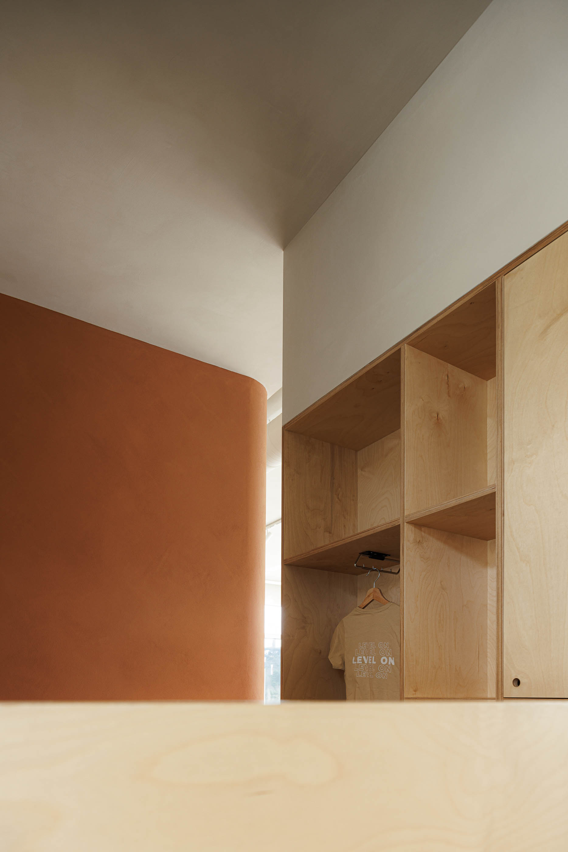 Vestiário: Armários em contraplacado, parede curva cor de tijolo, pavimento em madeira clara. — Level Private Gym arquitetura stu.dere em Penafiel