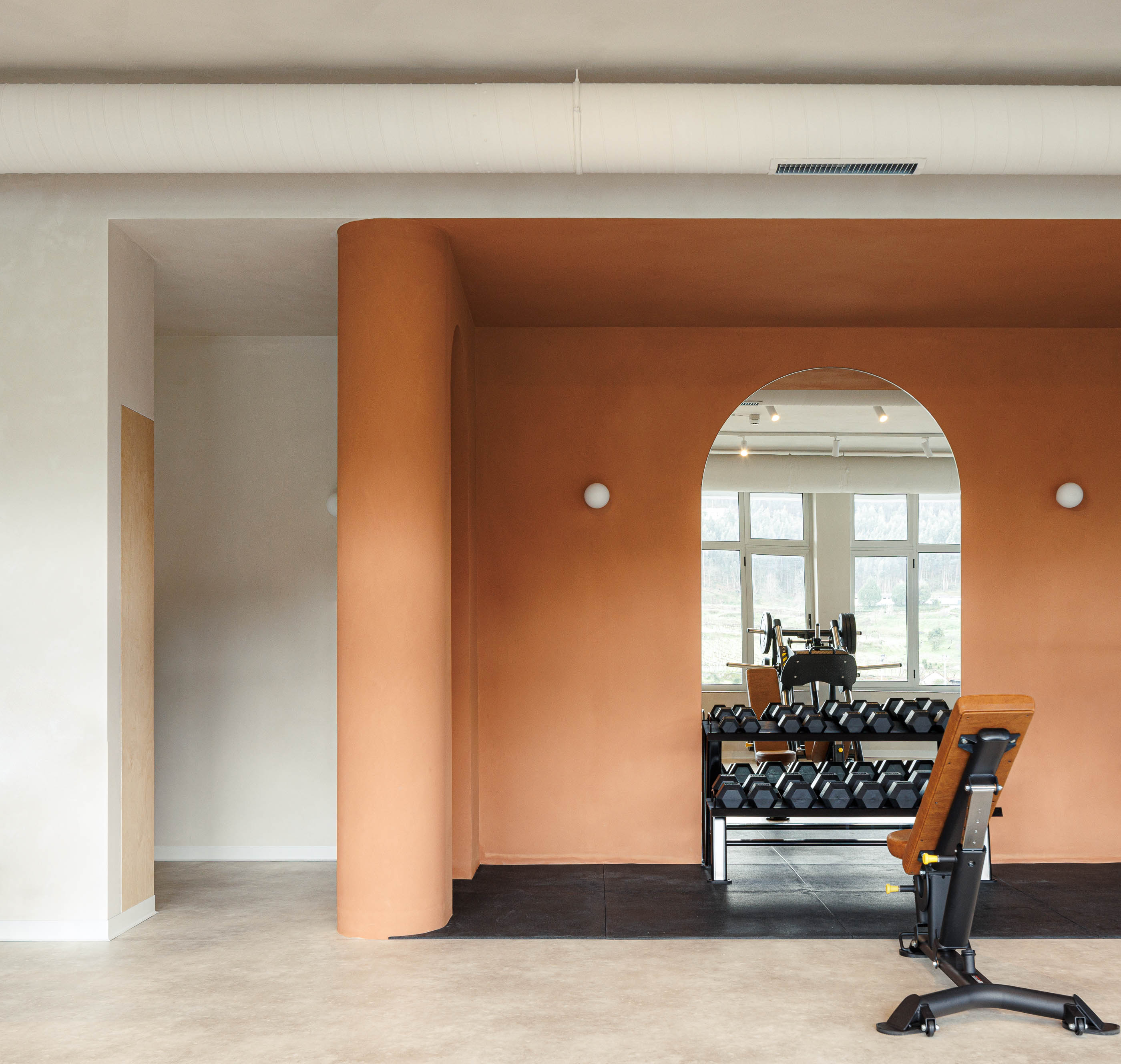 Zona de pesos: Parede cor de tijolo com nichos em arco, espelho, halteres e banco de musculação. — Level Private Gym arquitetura stu.dere em Penafiel