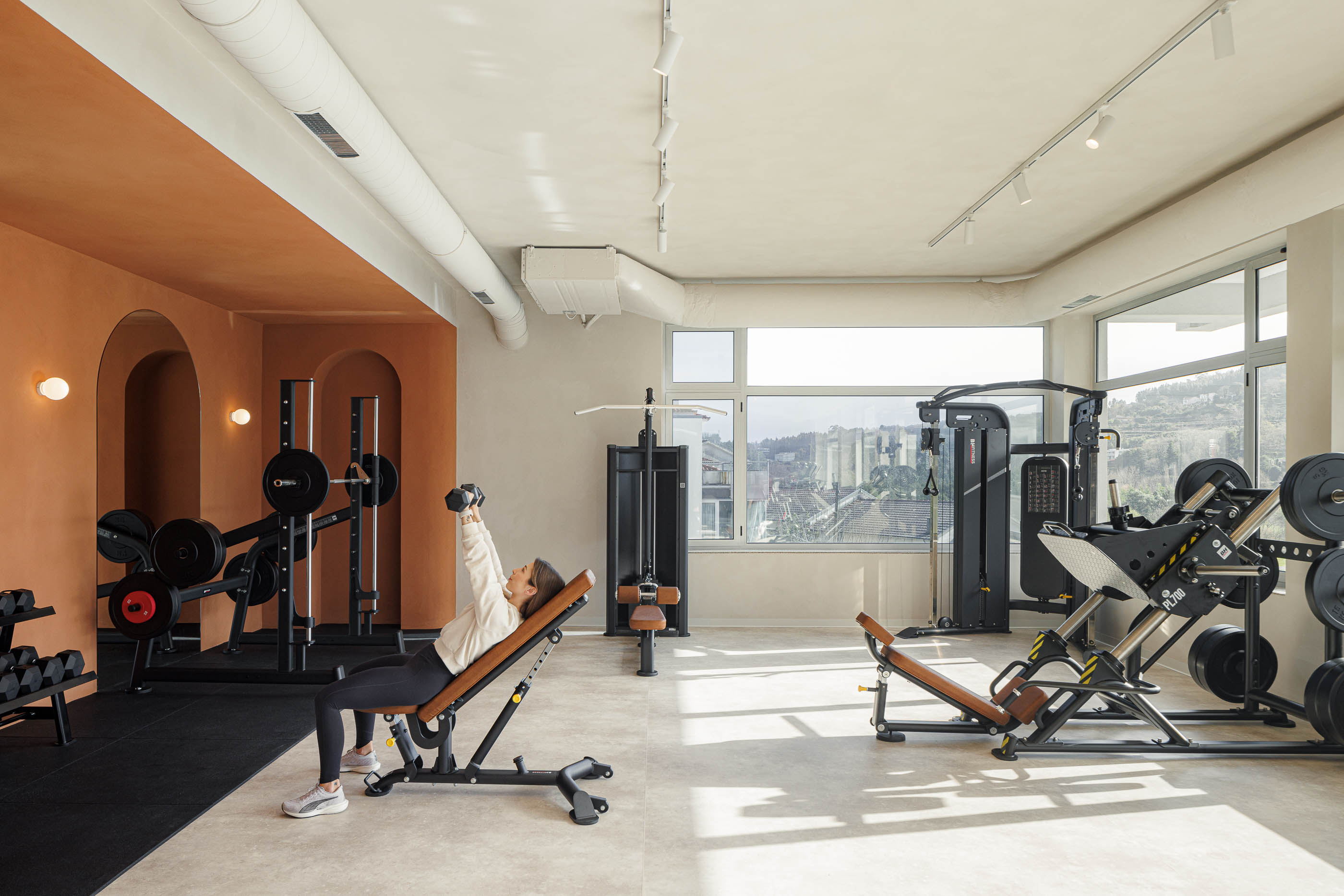 Sala de musculação: Equipamento de pesos, pavimento em borracha preta e pavimento cinzento, grandes janelas. — Level Private Gym arquitetura stu.dere em Penafiel