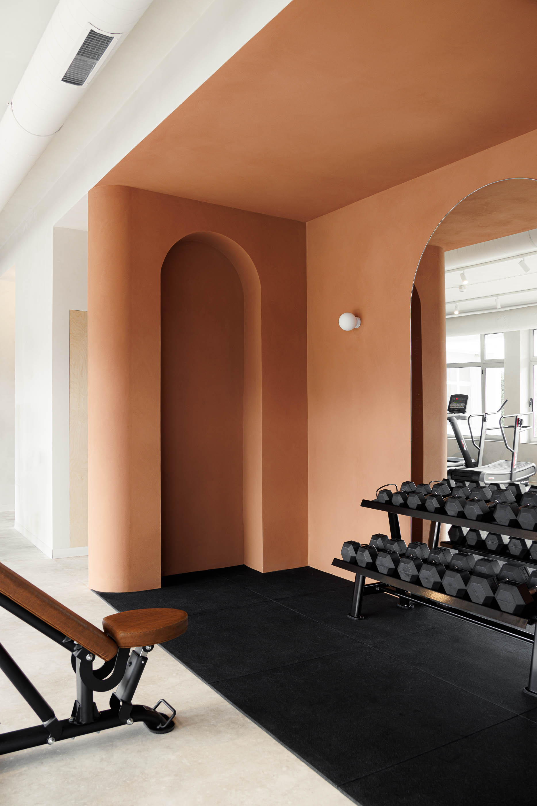 Zona de pesos: Halteres, banco de musculação, parede cor de tijolo com nichos em arco e espelho. — Level Private Gym arquitetura stu.dere em Penafiel