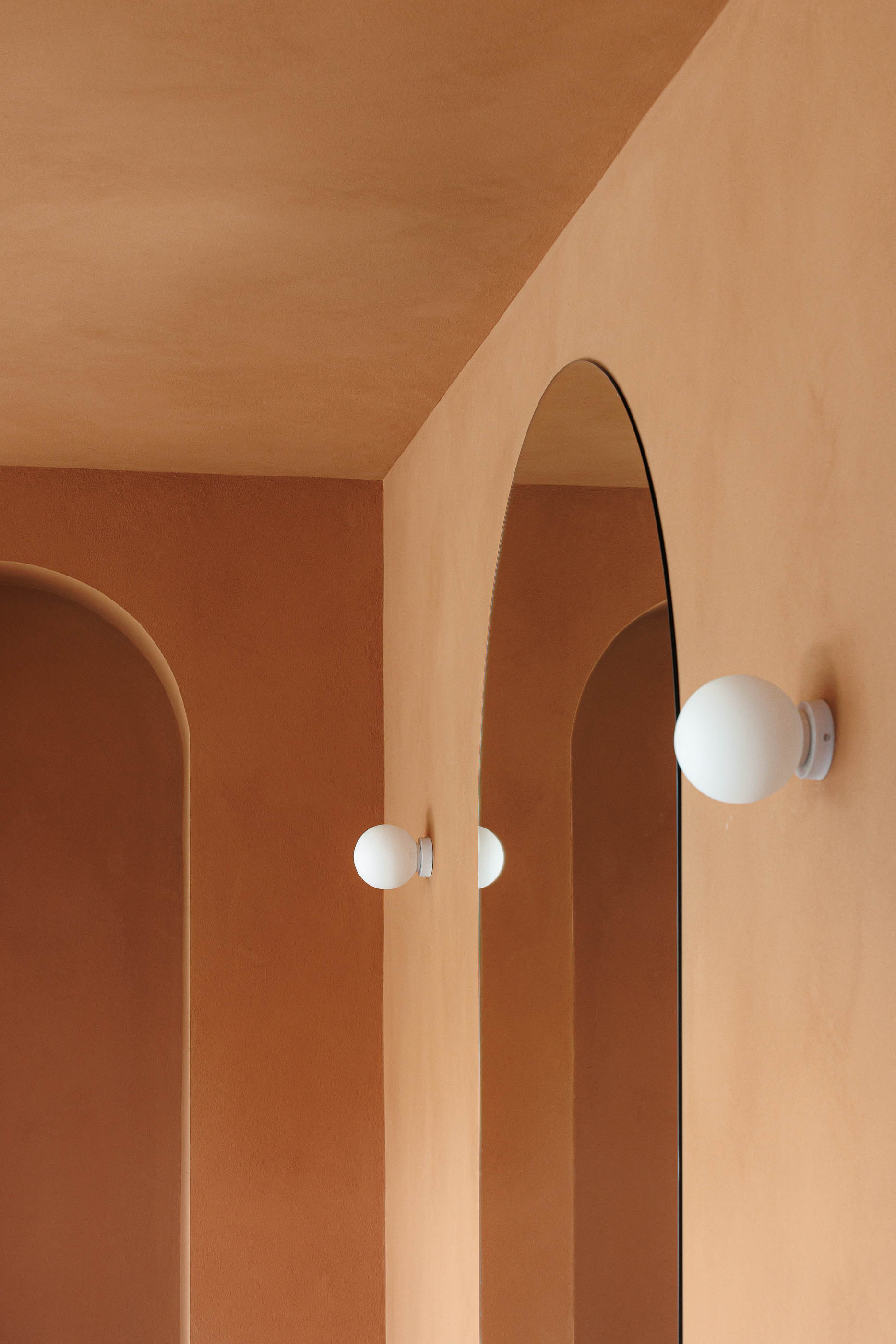 Detalhe: Espelho, candeeiro de parede esférico, parede cor de tijolo com nichos em arco. — Level Private Gym arquitetura stu.dere em Penafiel