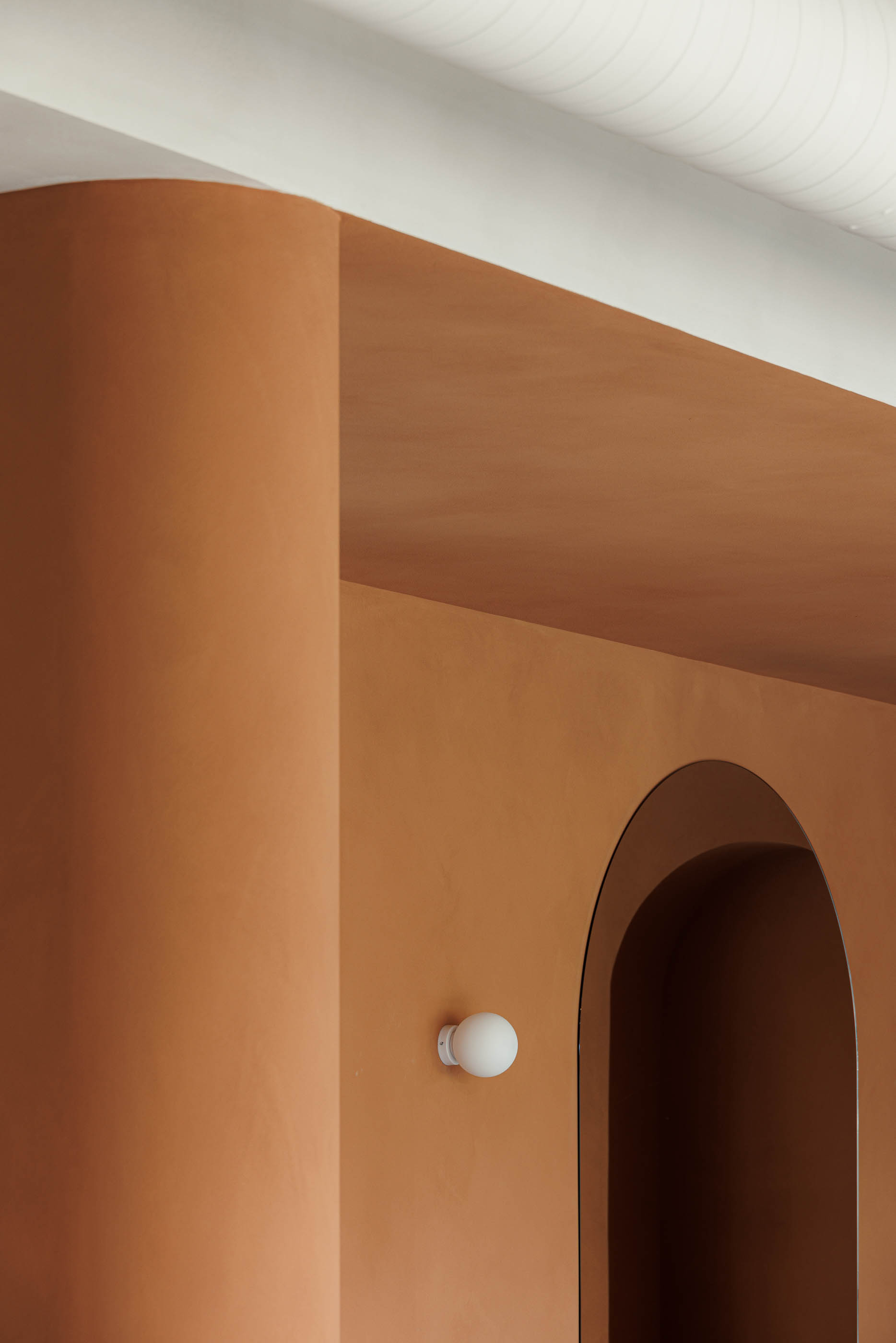 Detalhe: Coluna cor de tijolo, candeeiro de parede esférico, parede cor de tijolo com nicho em arco. — Level Private Gym arquitetura stu.dere em Penafiel