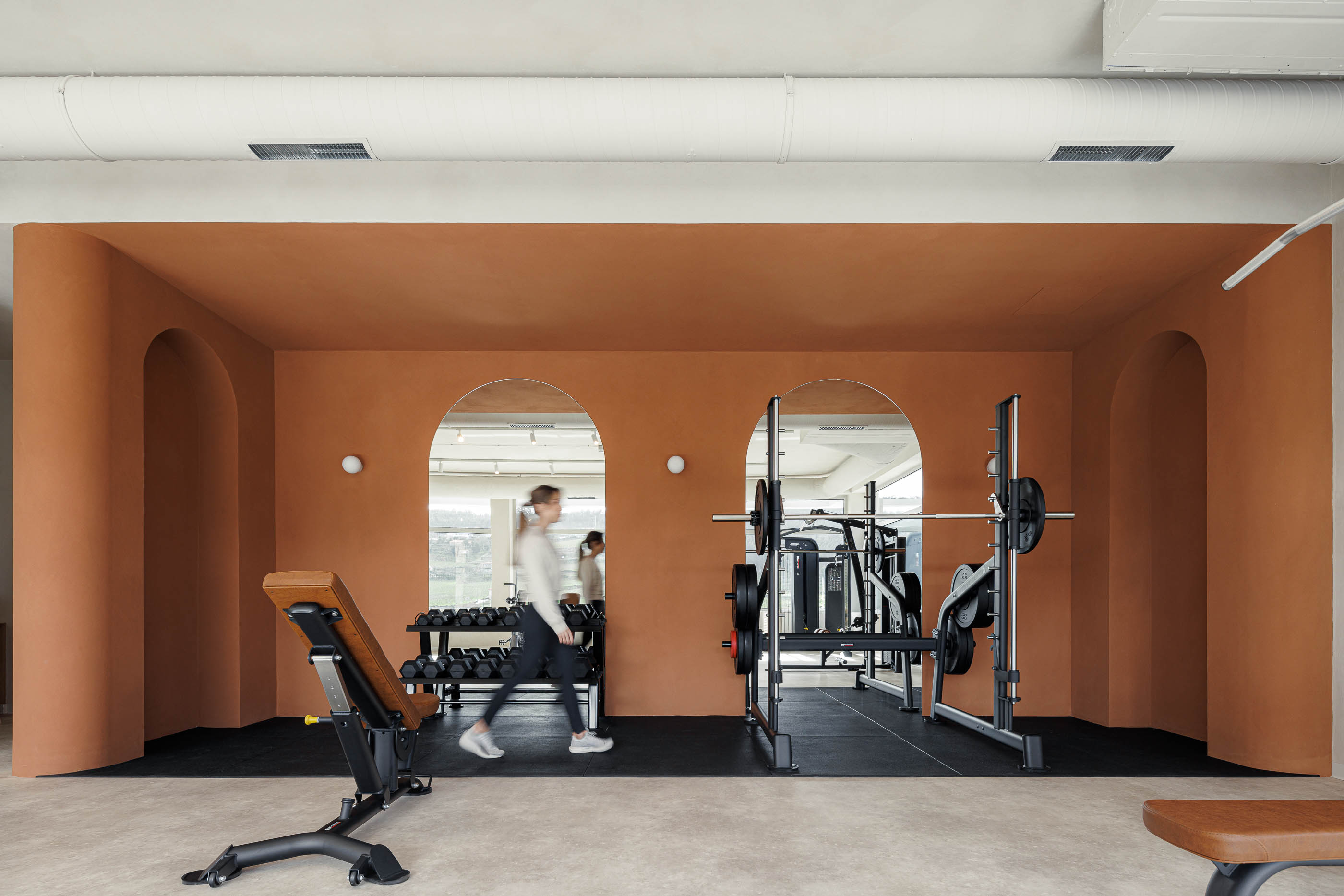 Sala de musculação: Equipamento de pesos, parede cor de tijolo com nichos em arco e espelhos. — Level Private Gym arquitetura stu.dere em Penafiel