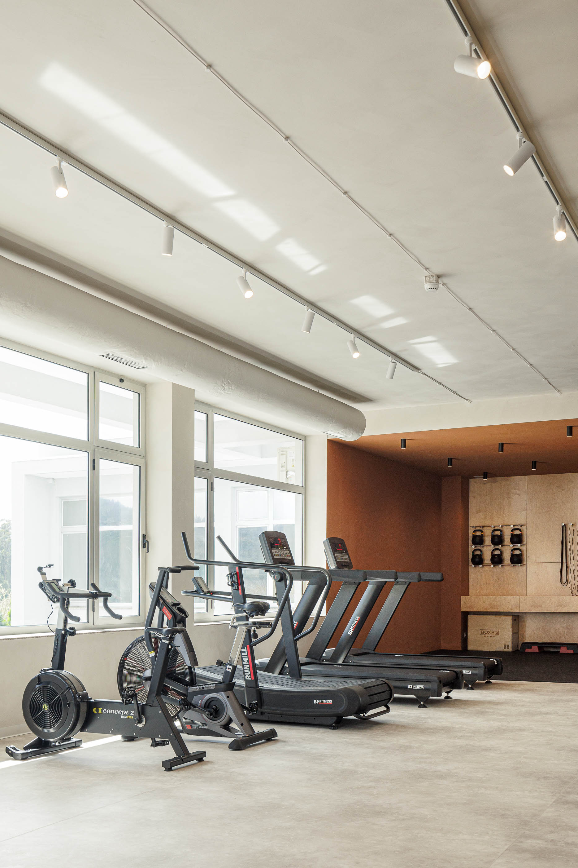 Sala de cardio: Passadeiras, bicicleta de spinning, pavimento cinzento, parede cor de tijolo ao fundo. — Level Private Gym arquitetura stu.dere em Penafiel
