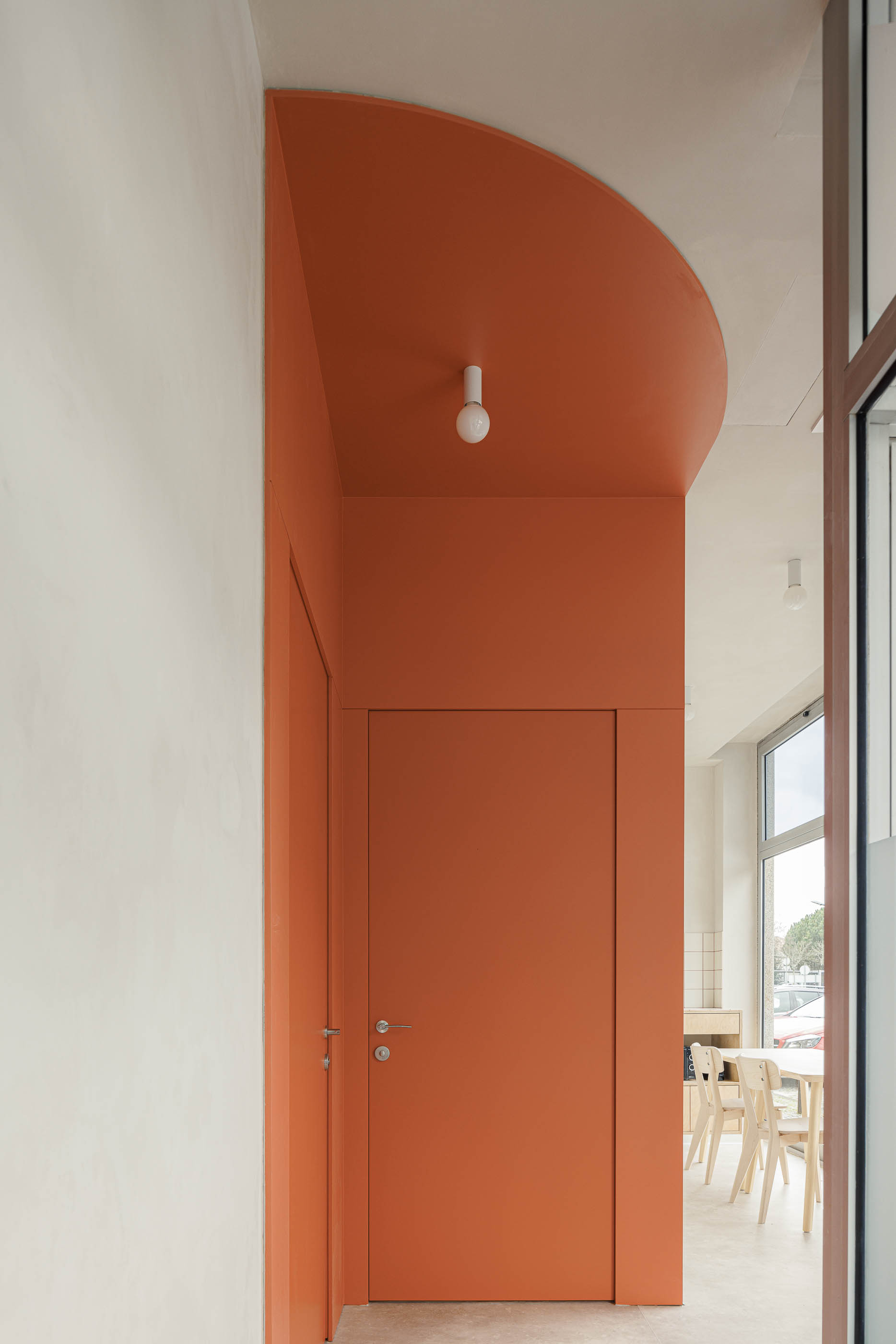 Detalhe: Porta cor de tijolo, candeeiro esférico, parede branca. — Level Private Gym arquitetura stu.dere em Penafiel