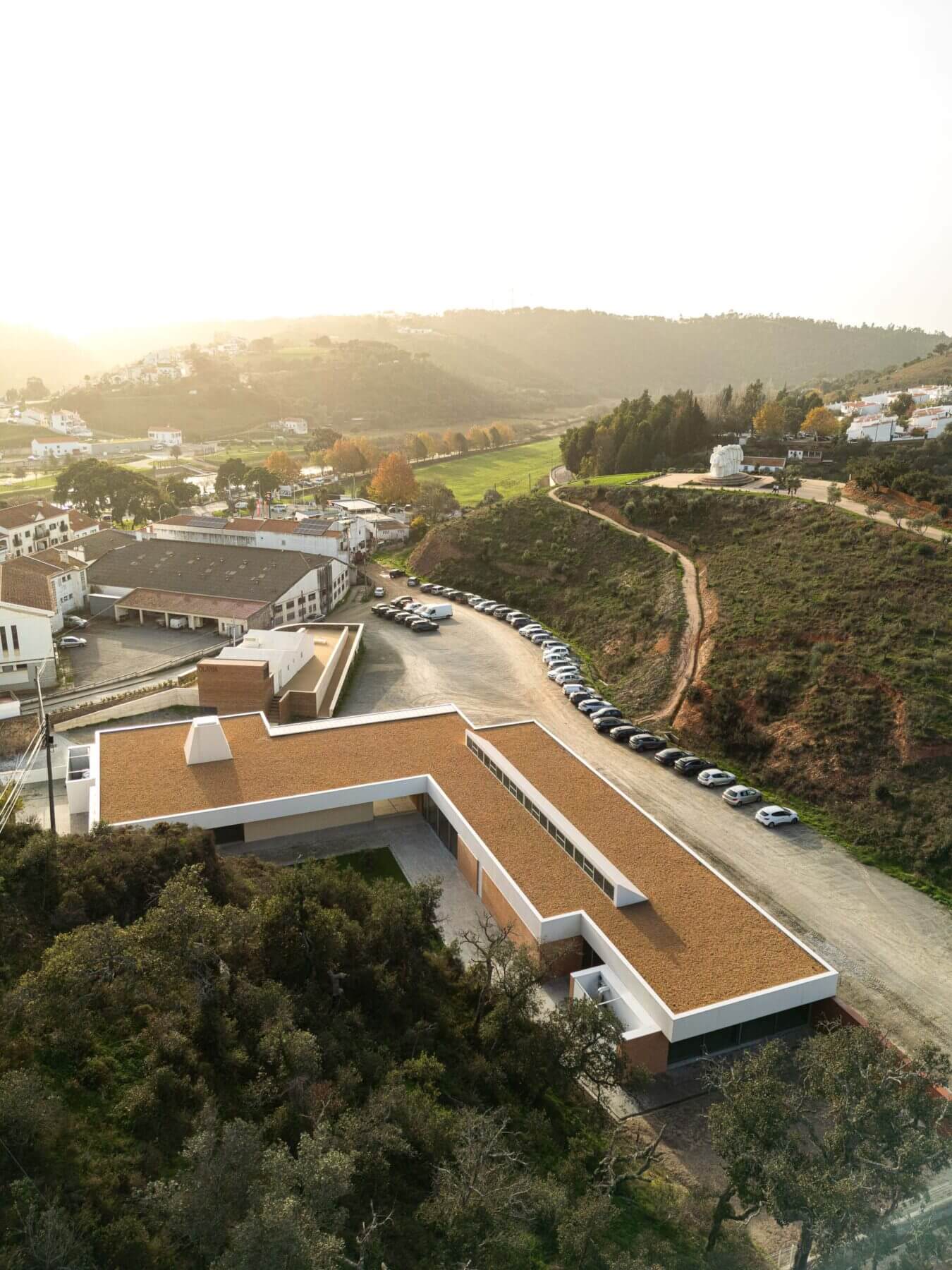 Edifício: Vista aérea da APCO com a paisagem de Odemira ao fundo, destacando o telhado castanho e a forma em "L". — Associação Paralisia Cerebral de Odemira – APCO arquitetura Filipe Xavier Oliveira em Odemira