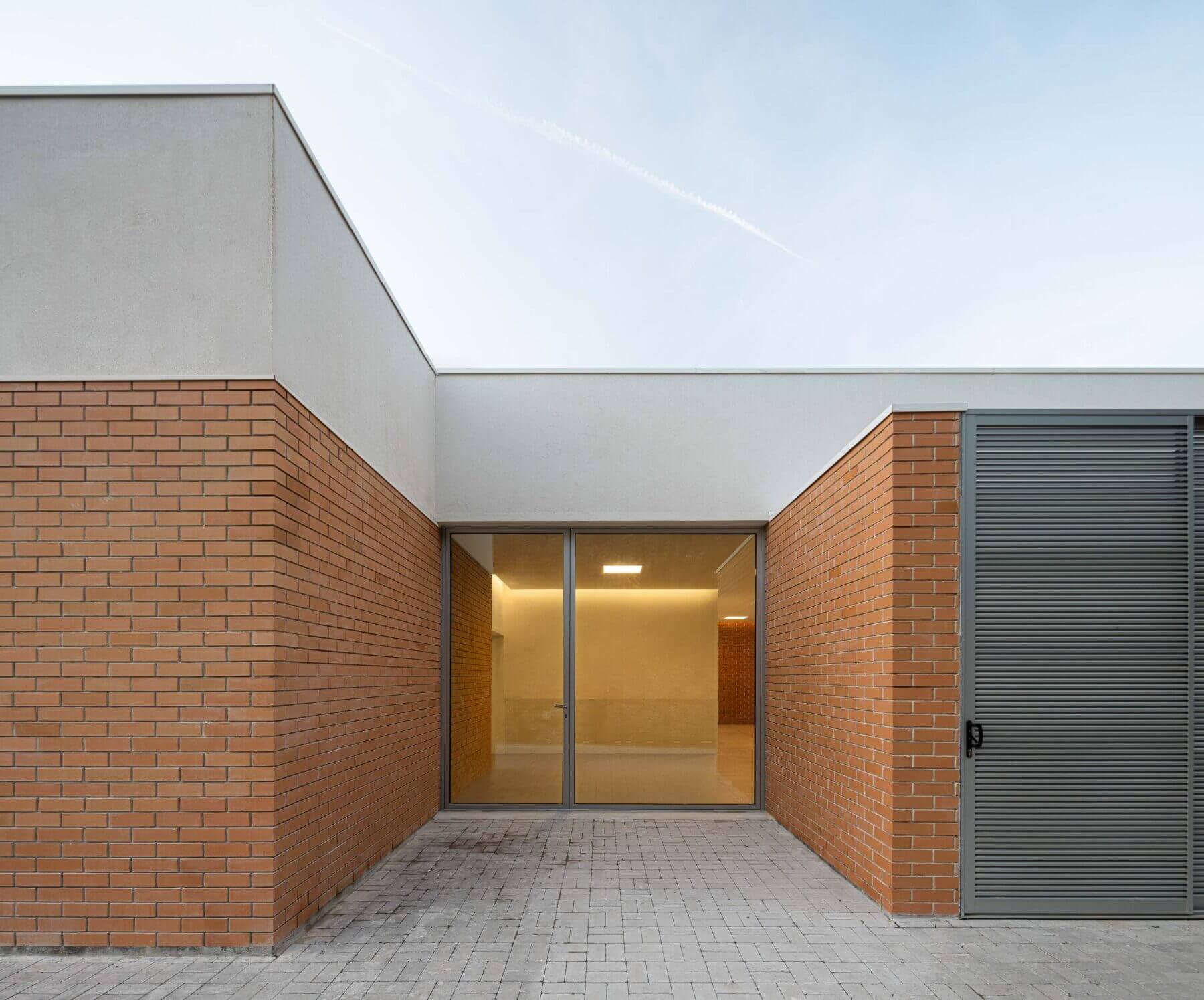 Pátio: Fachada em tijolo da APCO com grandes janelas e porta de acesso ao pátio exterior. — Associação Paralisia Cerebral de Odemira – APCO arquitetura Filipe Xavier Oliveira em Odemira