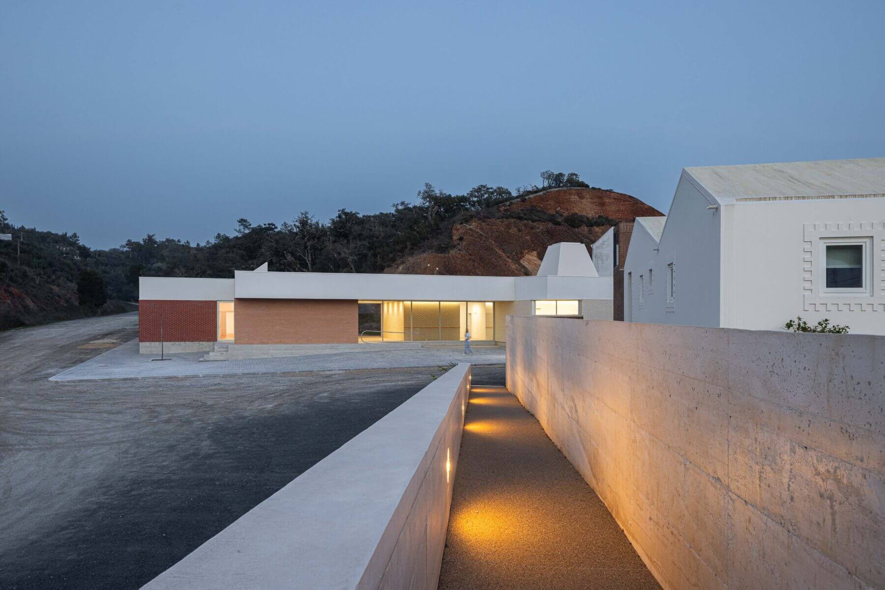 Edifício: Vista noturna da APCO, com iluminação embutida no caminho de acesso e fachada em tijolo. — Associação Paralisia Cerebral de Odemira – APCO arquitetura Filipe Xavier Oliveira em Odemira