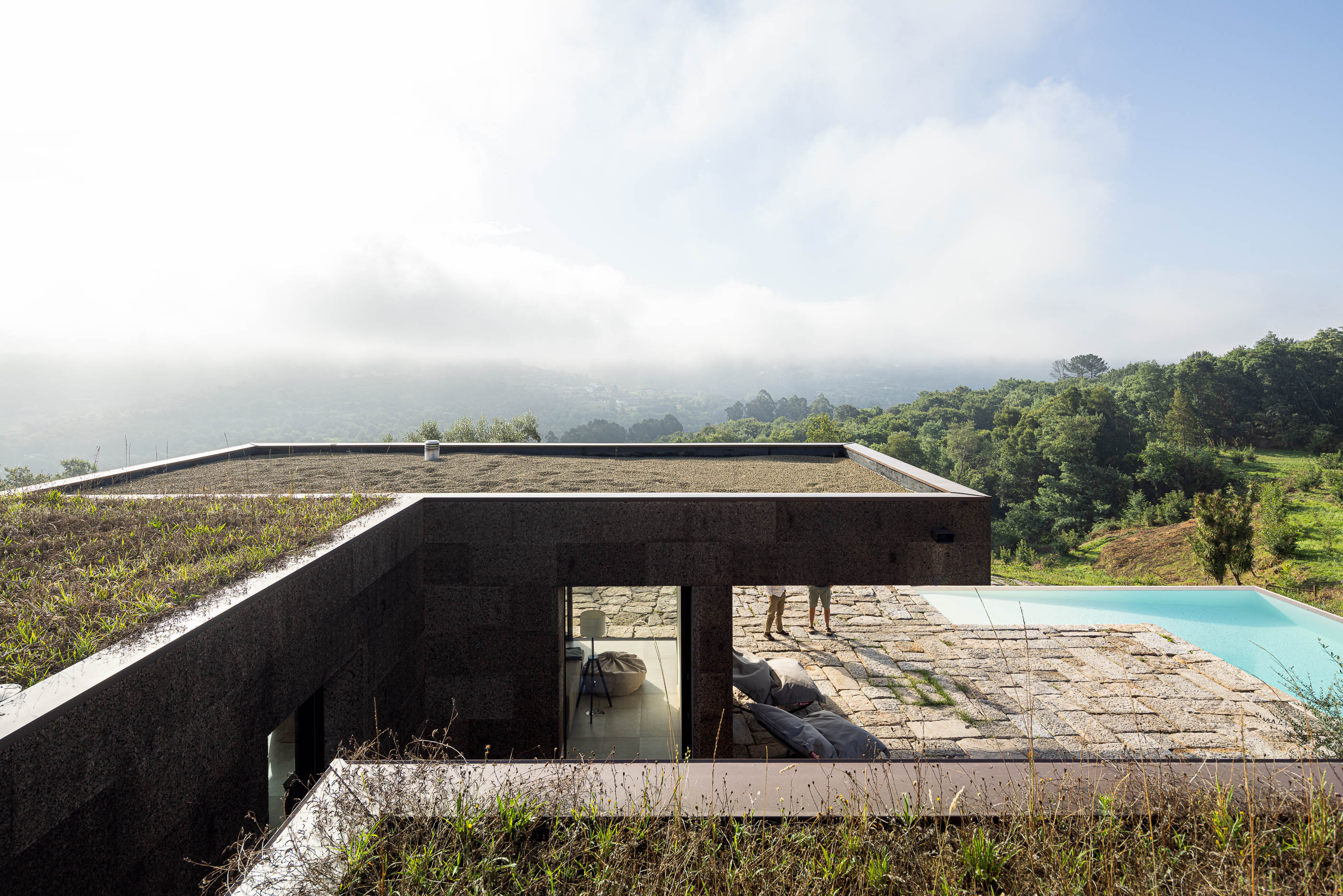 Exterior: Vista da casa com revestimento em cortiça, piscina e área de lazer com pavimento em pedra. — Casa da Levada arquitetura Tsou Arquitectos em Penafiel