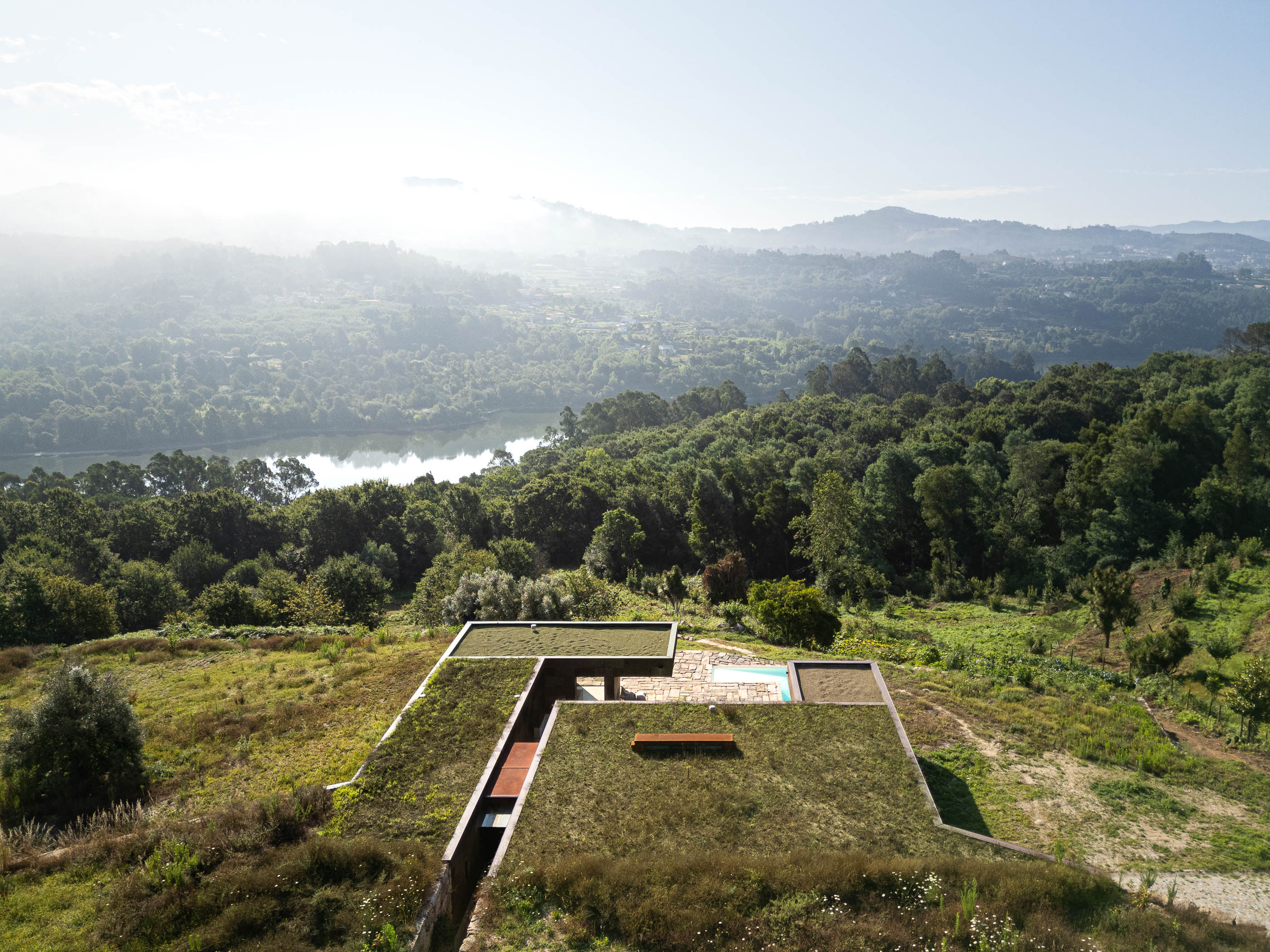 Exterior: Vista aérea da casa com telhado verde, piscina e paisagem natural envolvente. — Casa da Levada arquitetura Tsou Arquitectos em Penafiel