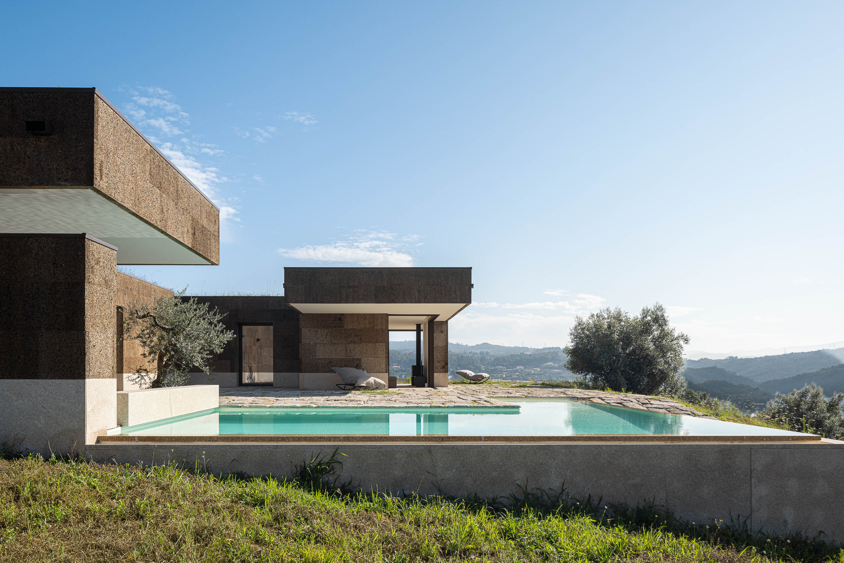 Exterior: Fachada da casa com piscina, revestimento em cortiça e pavimento em pedra. — Casa da Levada arquitetura Tsou Arquitectos em Penafiel