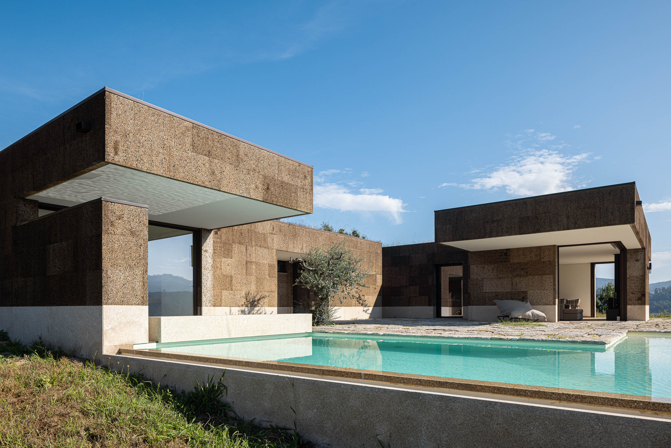 Exterior: Perspectiva da casa com piscina, revestimento em cortiça e base em pedra. — Casa da Levada arquitetura Tsou Arquitectos em Penafiel