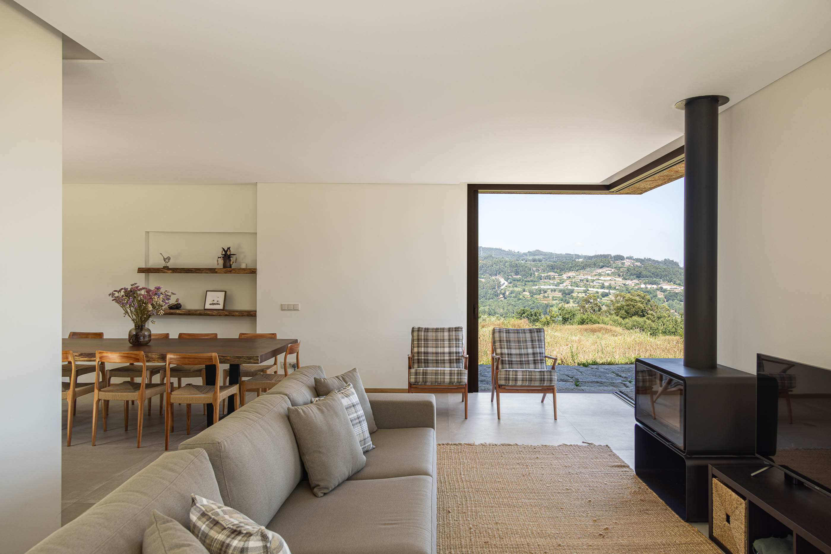 Sala de estar/jantar: Espaço amplo com sofá, cadeiras, mesa de jantar e lareira moderna. — Casa da Levada arquitetura Tsou Arquitectos em Penafiel