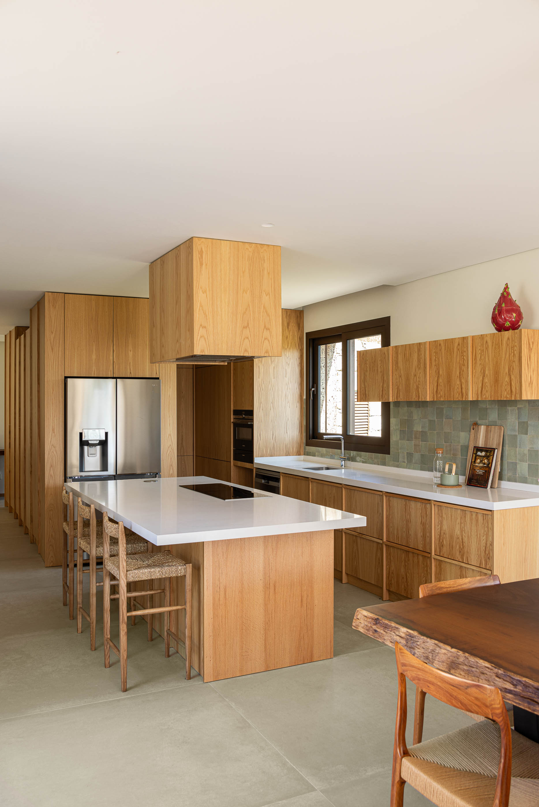 Cozinha: Armários em madeira clara, bancada branca e revestimento cerâmico verde. — Casa da Levada arquitetura Tsou Arquitectos em Penafiel