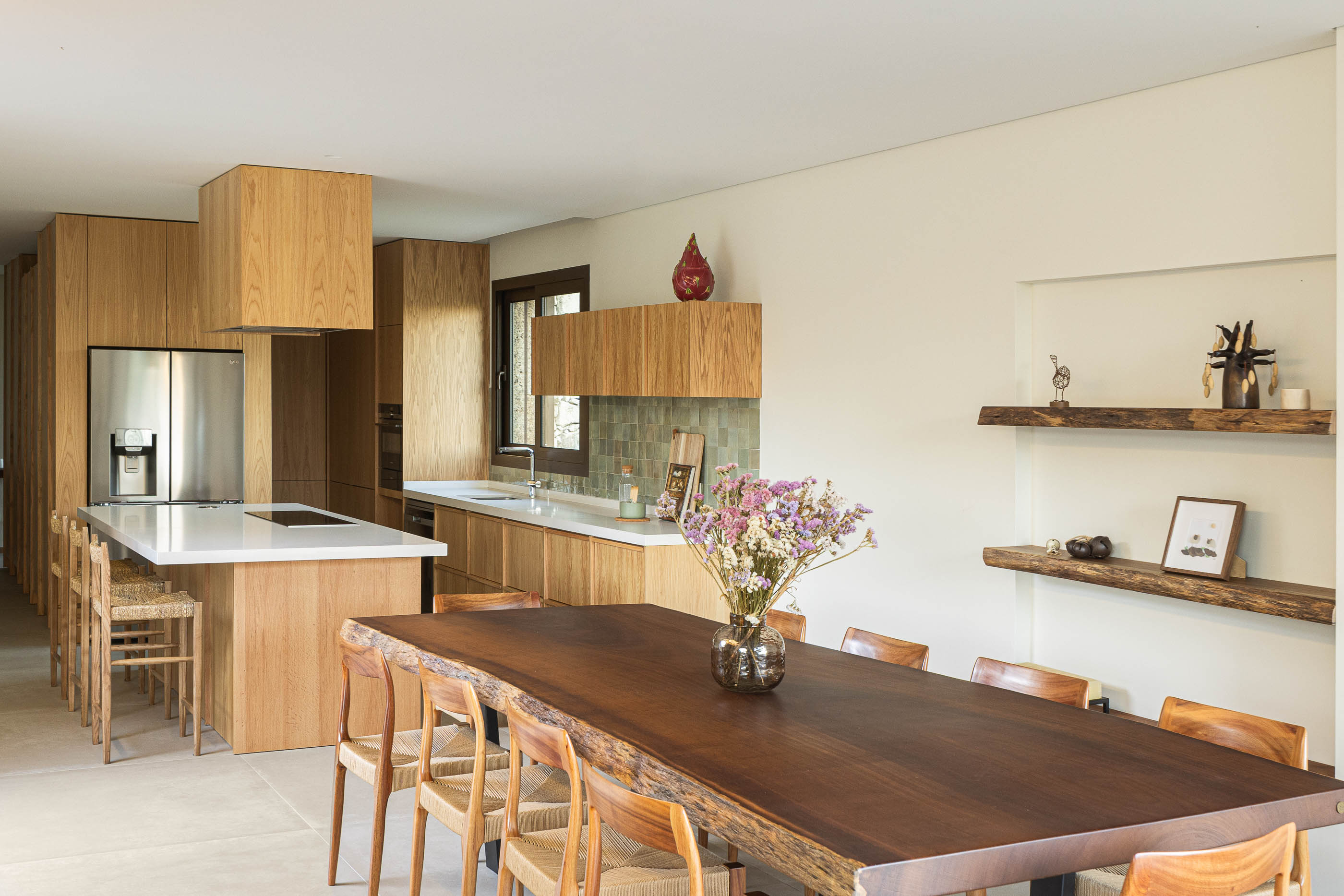 Cozinha/sala de jantar: Mesa de jantar em madeira maciça e cozinha com armários em madeira clara. — Casa da Levada arquitetura Tsou Arquitectos em Penafiel