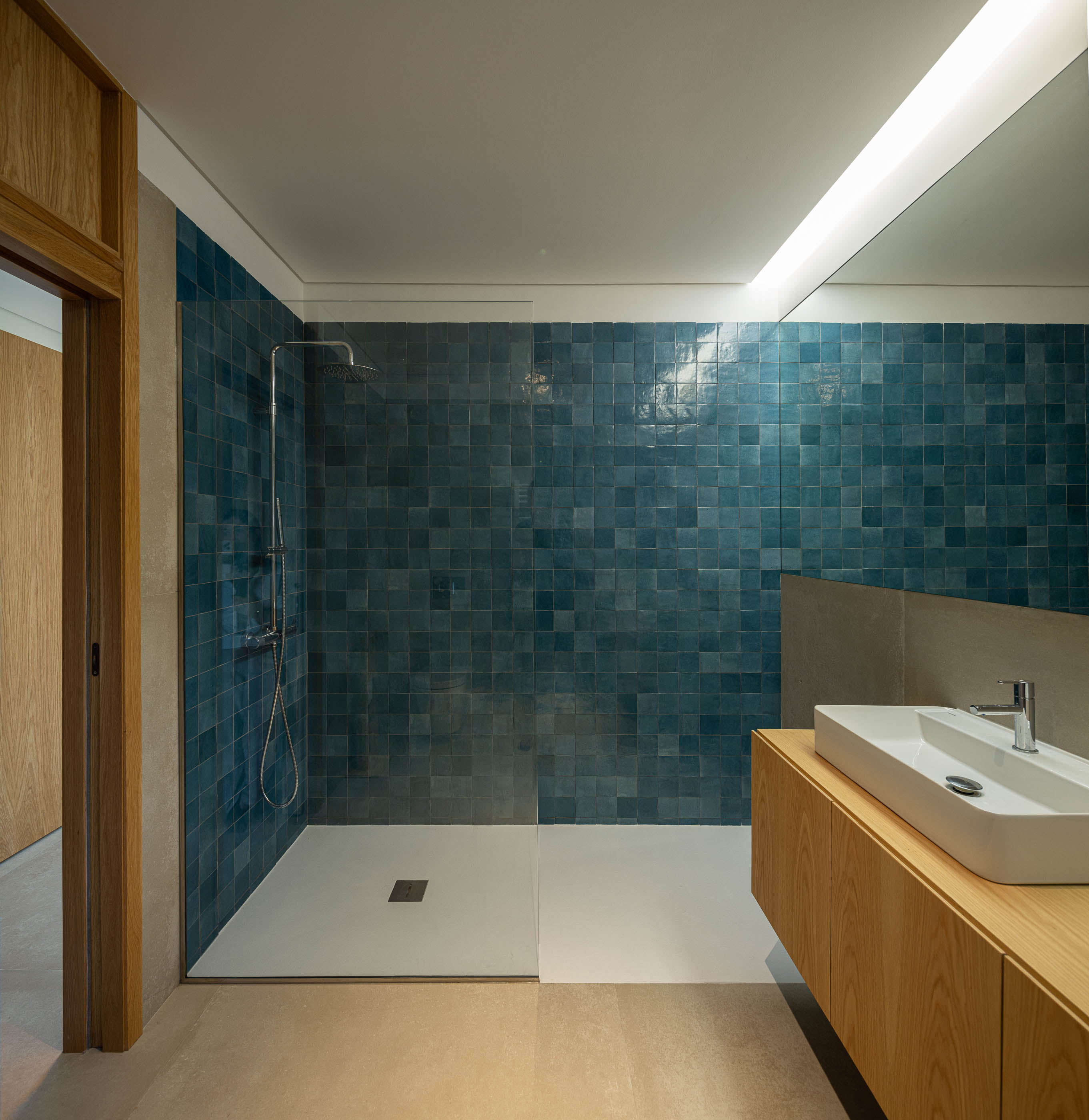 Casa de banho: Revestimento em azulejo azul, lavatório embutido em móvel de madeira clara e base de duche. — Casa da Levada arquitetura Tsou Arquitectos em Penafiel