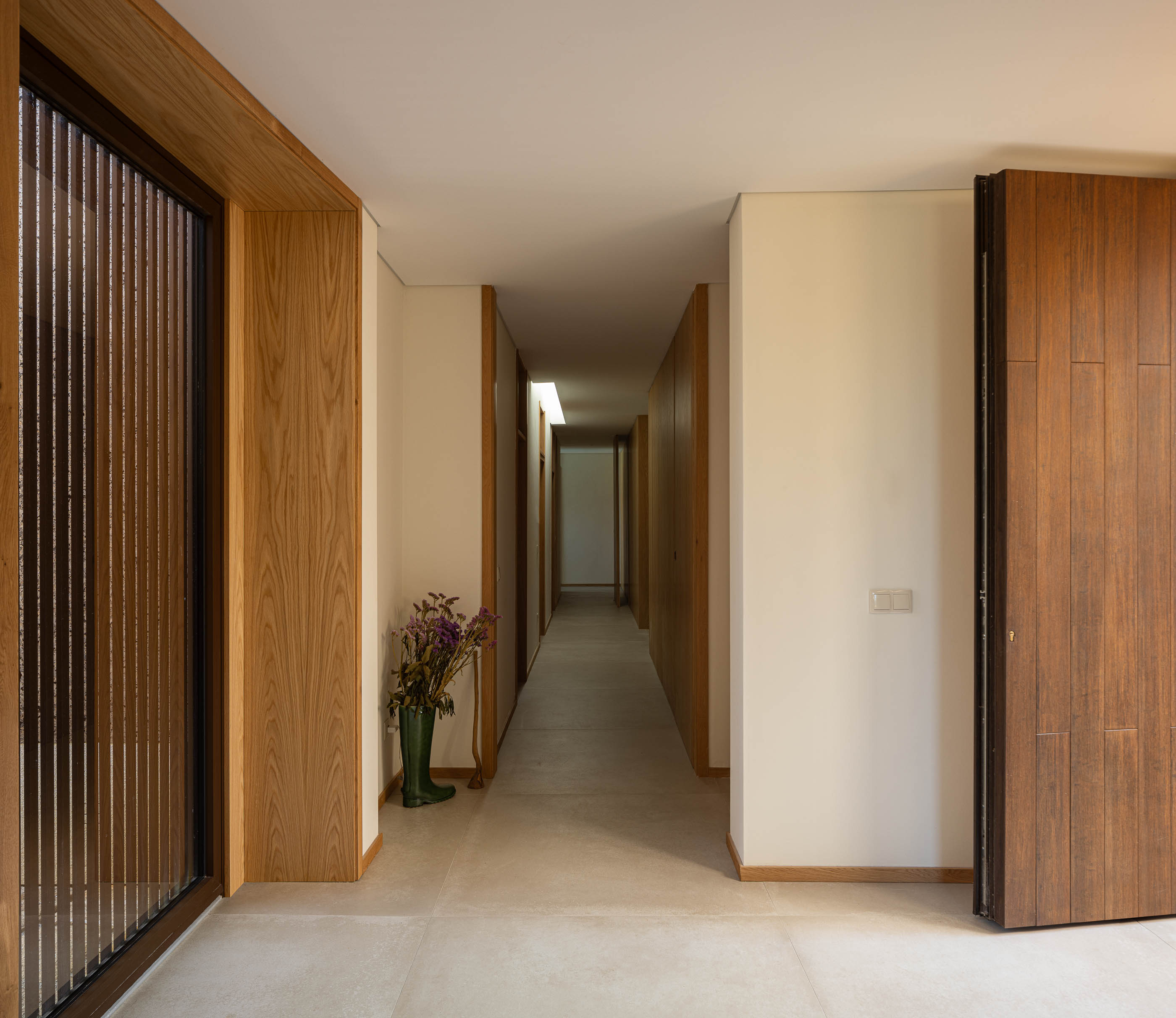 Corredor: Longo corredor com armários embutidos em madeira clara e pavimento em cerâmica. — Casa da Levada arquitetura Tsou Arquitectos em Penafiel