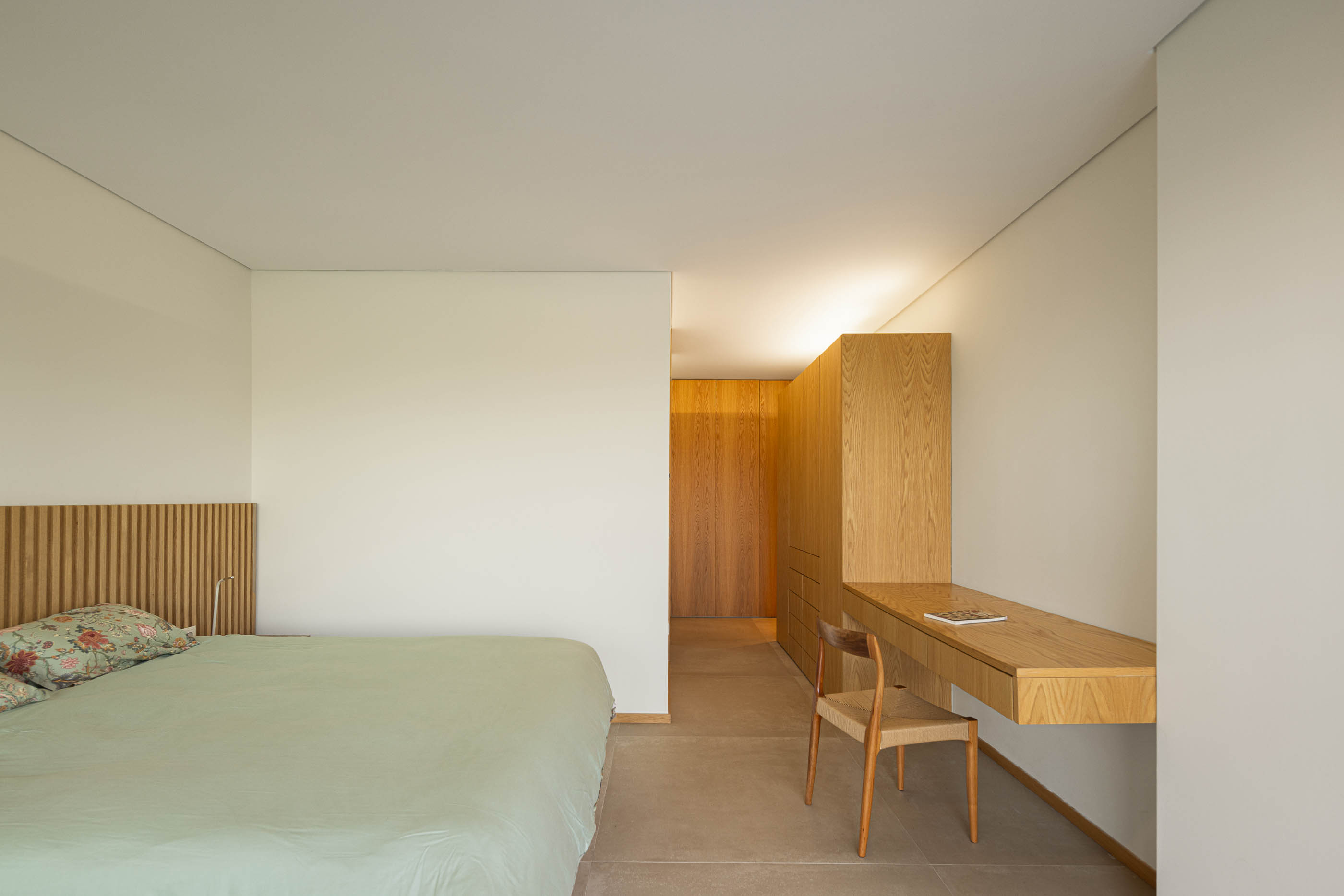 Quarto: Cama com cabeceira em madeira, secretária suspensa e armários em madeira clara. — Casa da Levada arquitetura Tsou Arquitectos em Penafiel