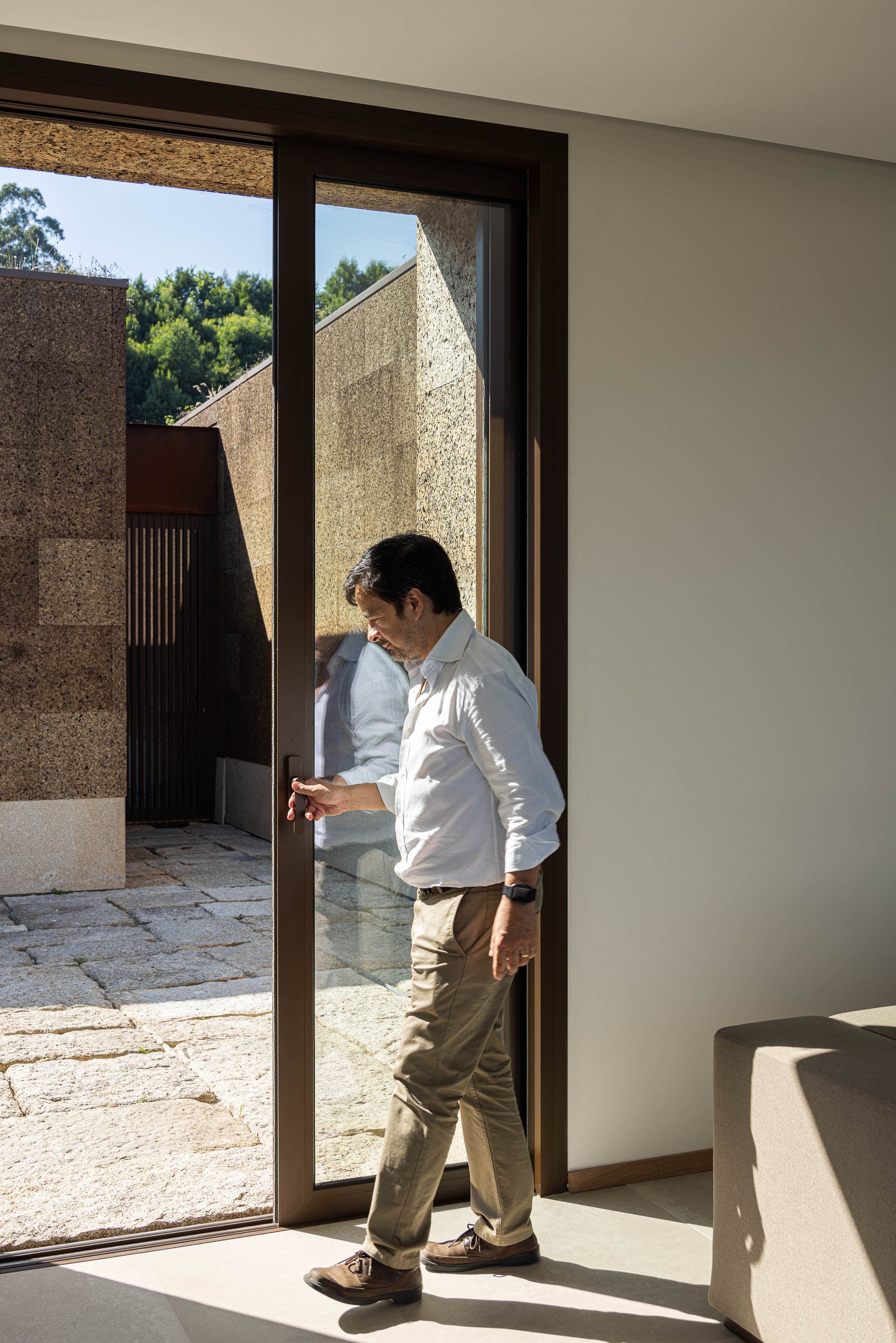 Sala de estar: Homem a abrir porta de correr com vista para o pátio exterior em pedra. — Casa da Levada arquitetura Tsou Arquitectos em Penafiel
