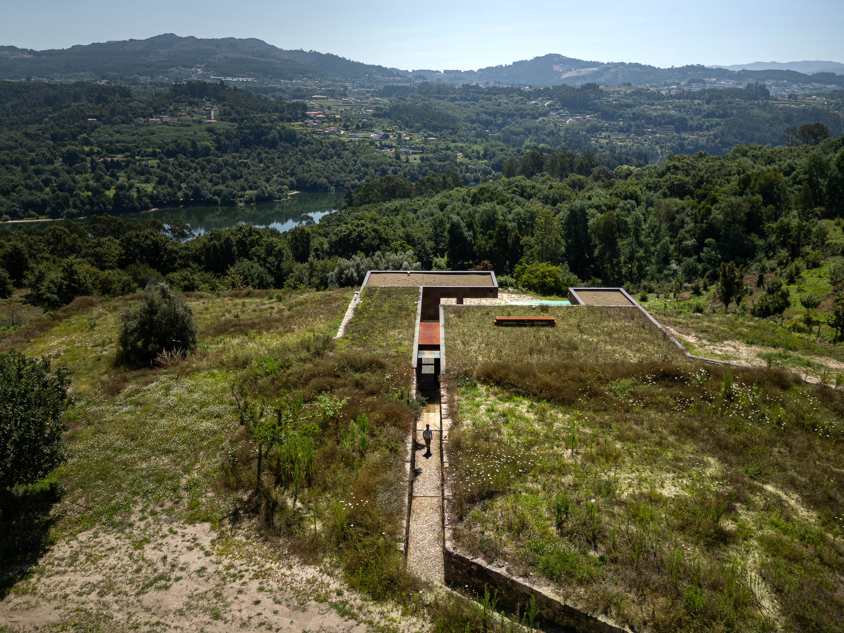 Exterior: Vista aérea da casa com telhado verde, passadiço de acesso e paisagem natural. — Casa da Levada arquitetura Tsou Arquitectos em Penafiel